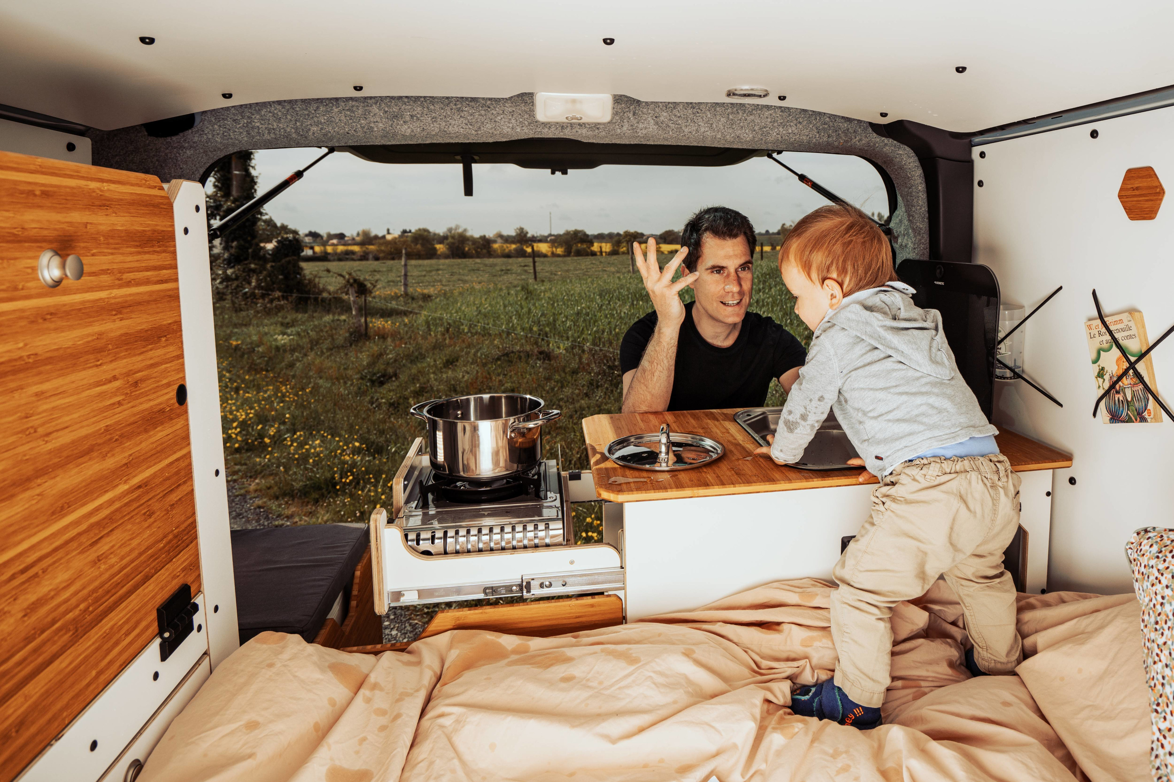 Dad and child enjoy their **RV rental** camper van, featuring a compact kitchen & cozy bed for family adventures.. Renault Trafic 2025