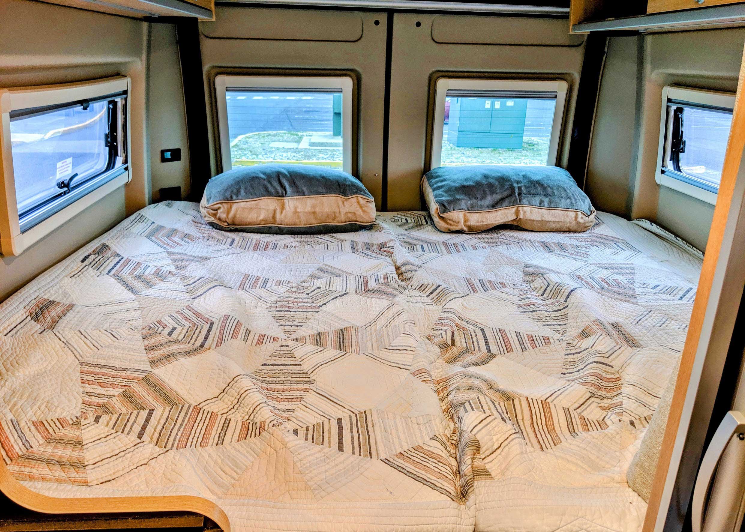 Cozy RV rental bedroom with a patterned quilt, two pillows, and windows.. Hymer Aktiv 2.0 2019