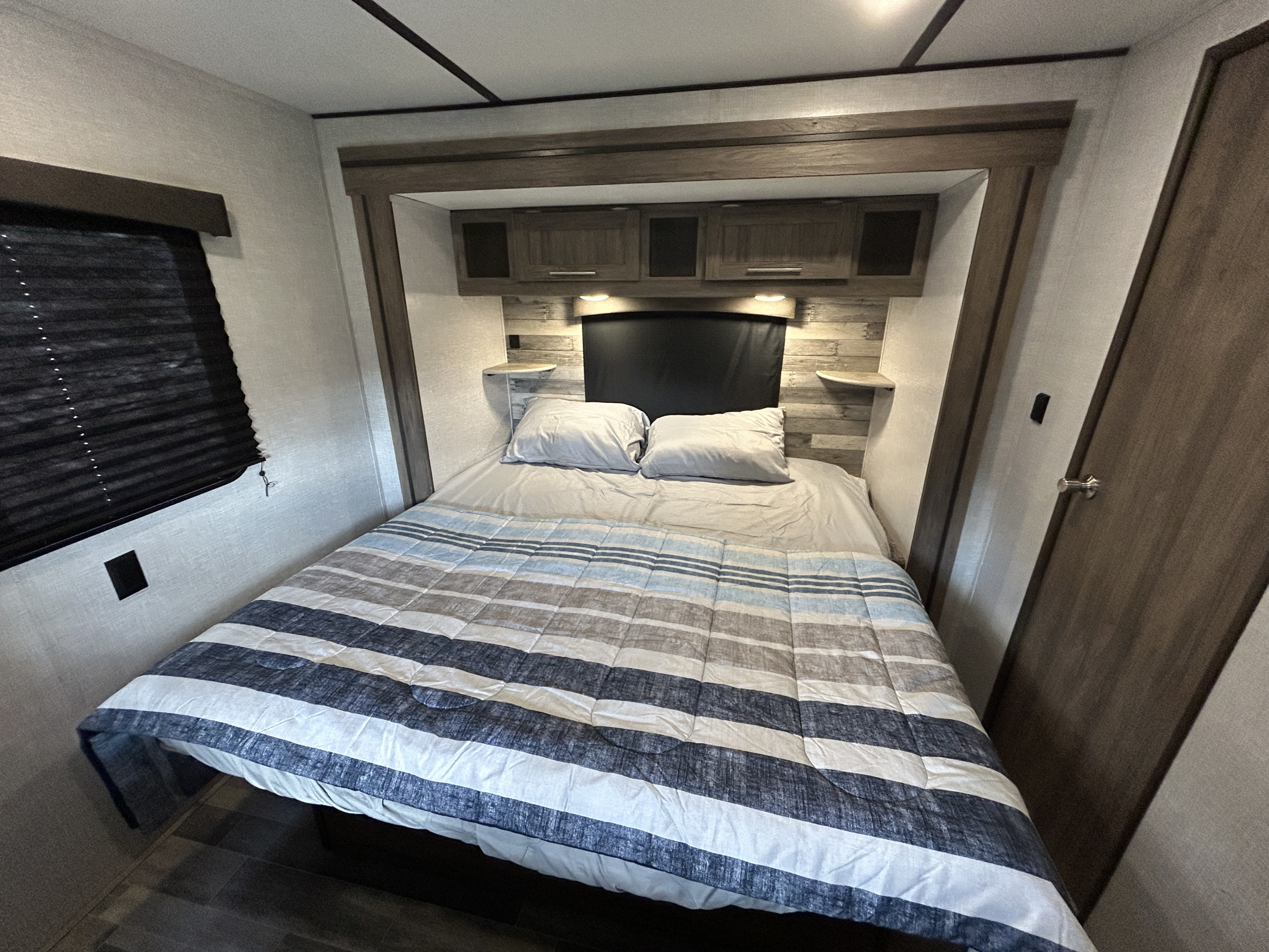 RV rental bedroom with a comfy striped bed, overhead storage, and shelves, ready for your next adventure.. Crossroads Zinger 2021