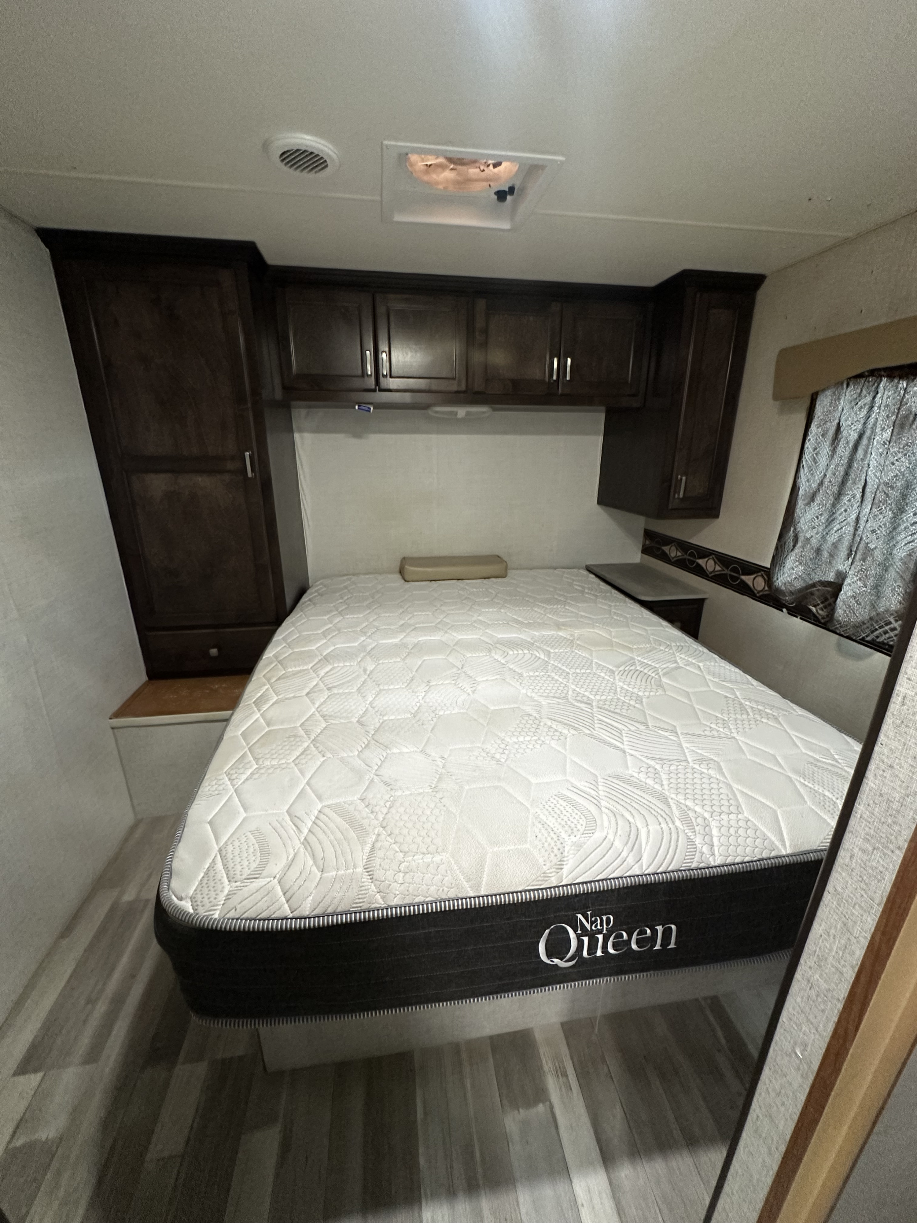 Cozy RV rental bedroom features a Nap Queen mattress, dark wood cabinets, and a side window.. Winnebago Minnie Winnie 2015