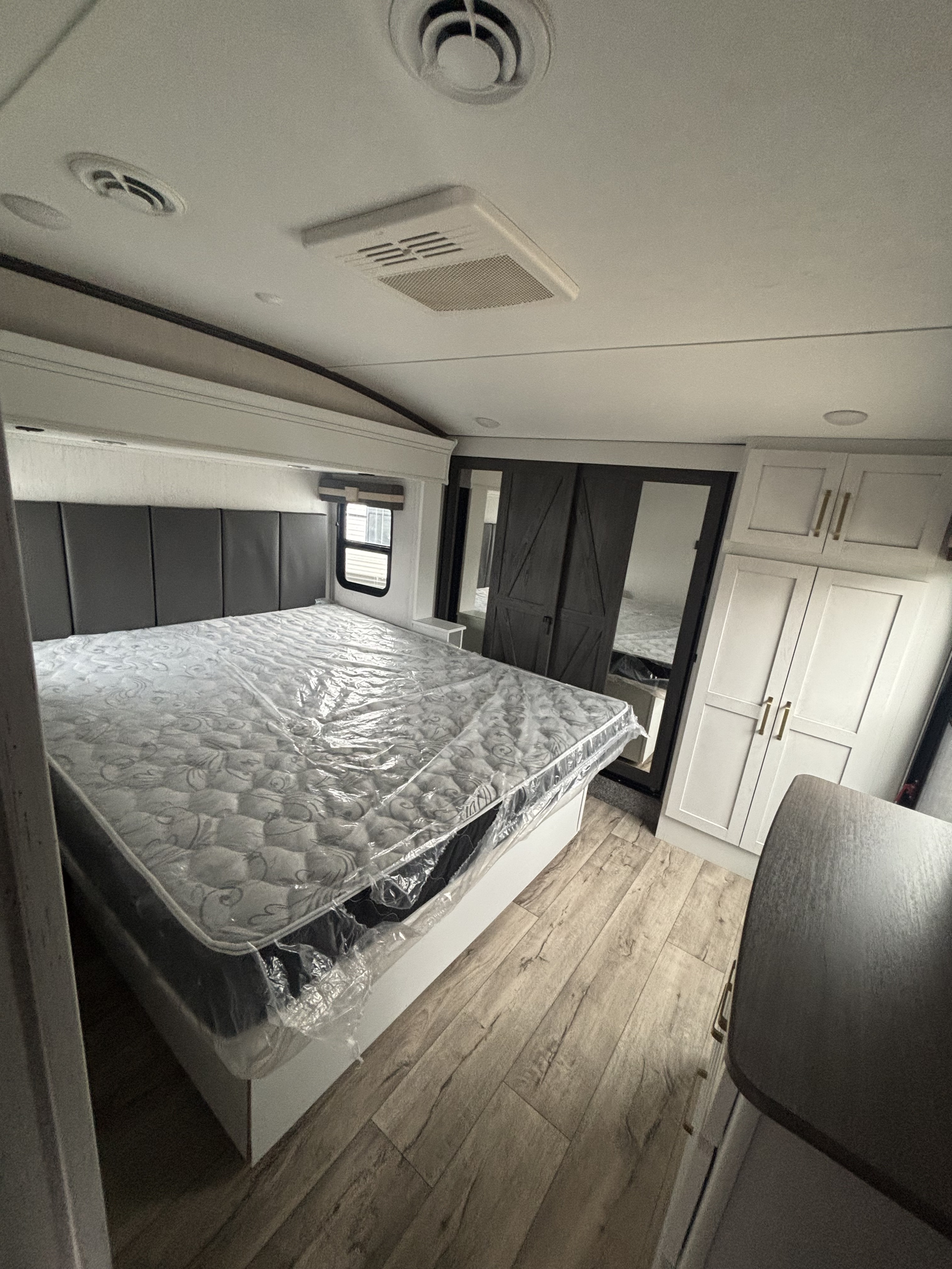 New RV rental bedroom: large bed with wrapped mattress, barn door wardrobe, white cabinets, and wood-look floor.. Keystone Astoria 2023