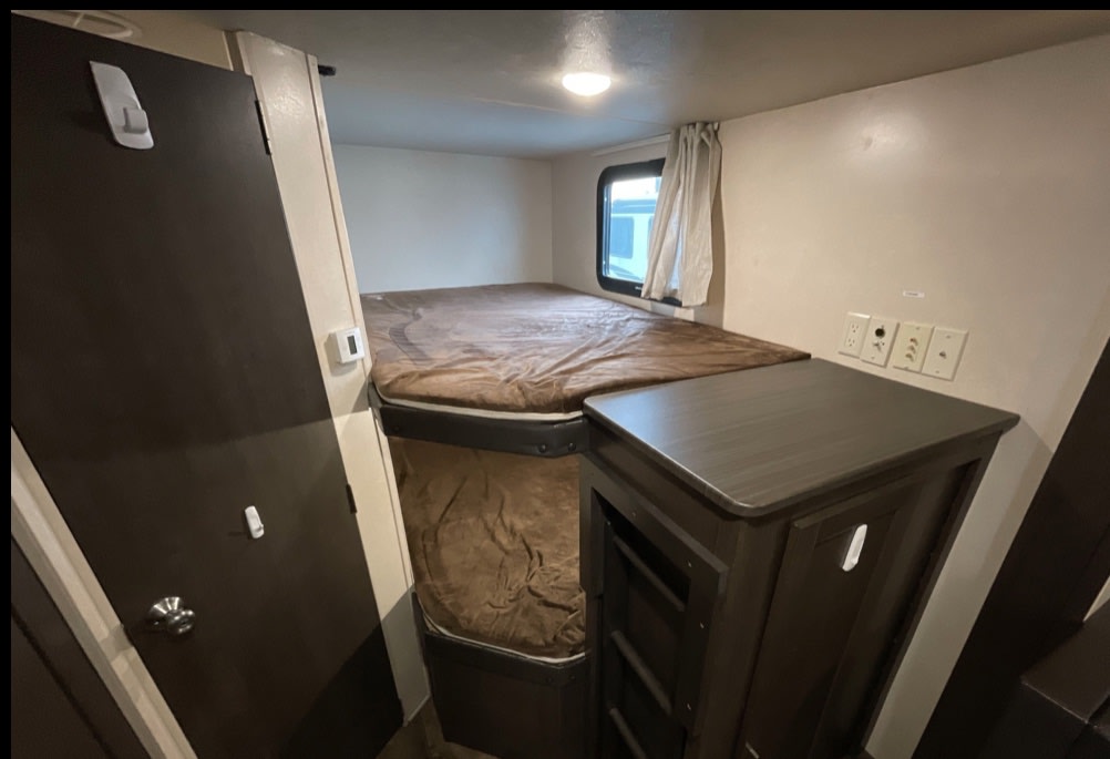 Cozy RV rental bunk beds and compact sleeping area, perfect for travel. See wall outlets and storage cabinet.. Forest River Wildwood X-Lite 2020