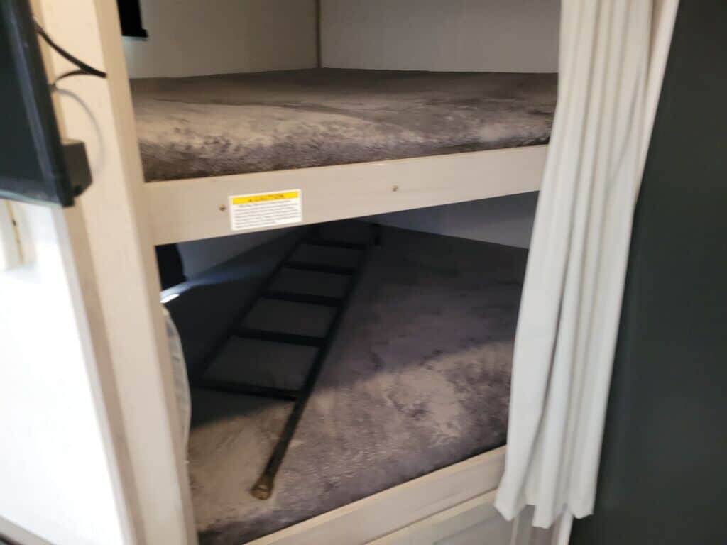 Inside this RV rental, cozy bunk beds with soft mattresses, a ladder, TV, and privacy curtain offer comfortable travel lodging.. Keystone Kodiak 2022
