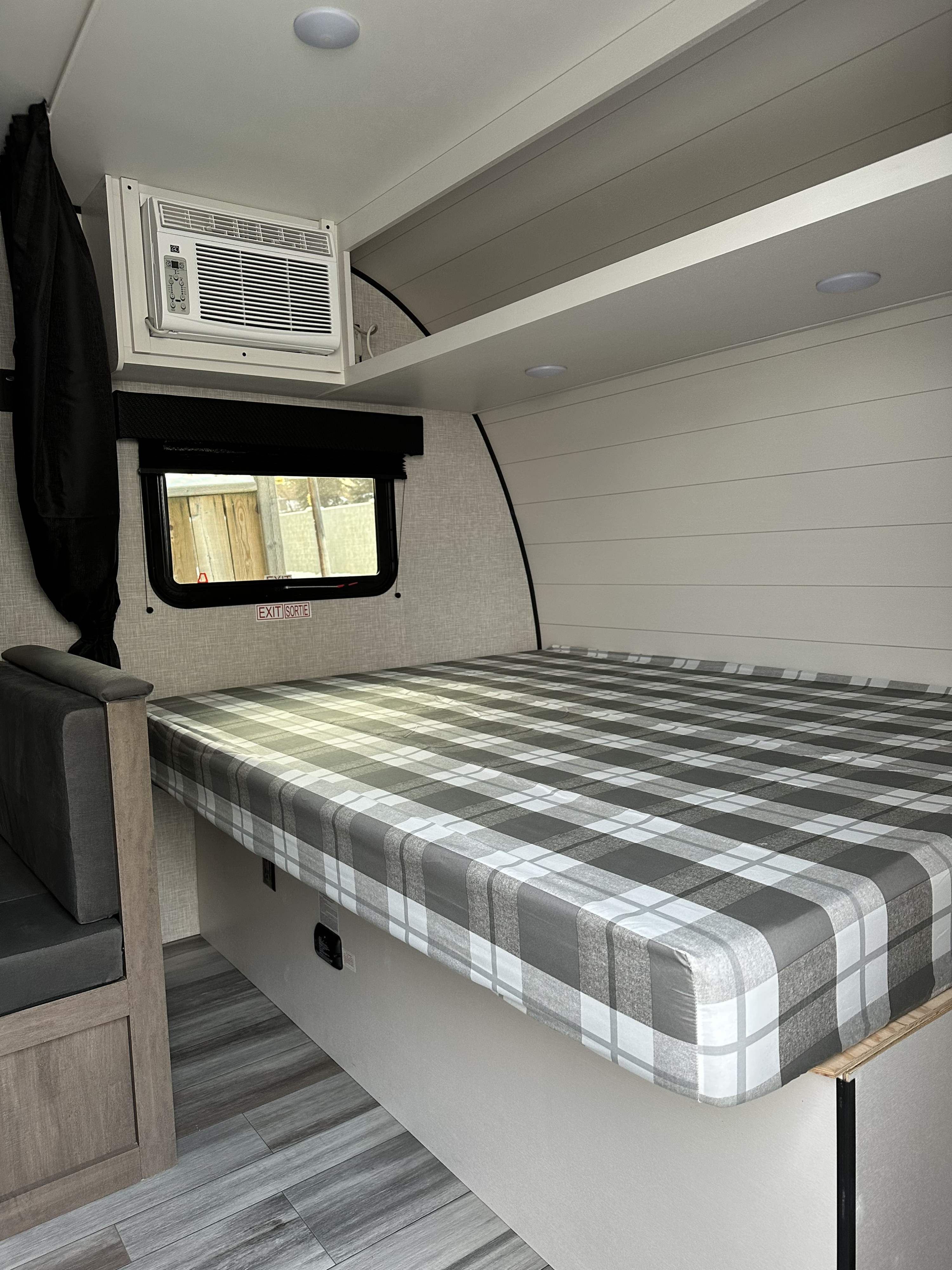Modern RV rental interior with a grey plaid bed, compact AC unit, window, and overhead storage.. Jayco Jayflight SLX 175BHW Baja 2025
