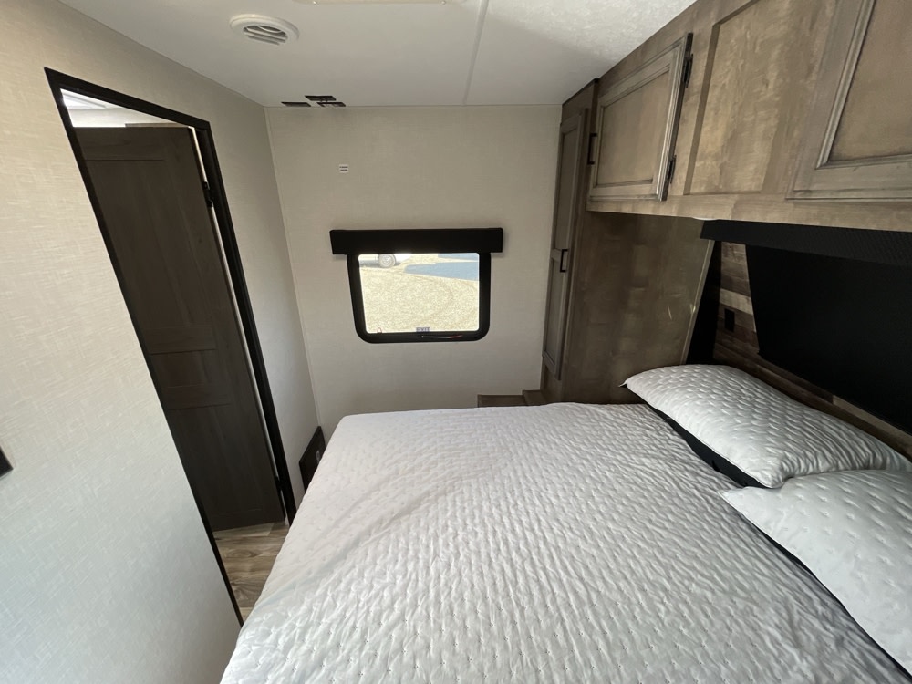 RV rental bedroom with a white bed, overhead cabinets, and a side window providing natural light.. Venture 327VIK 2024