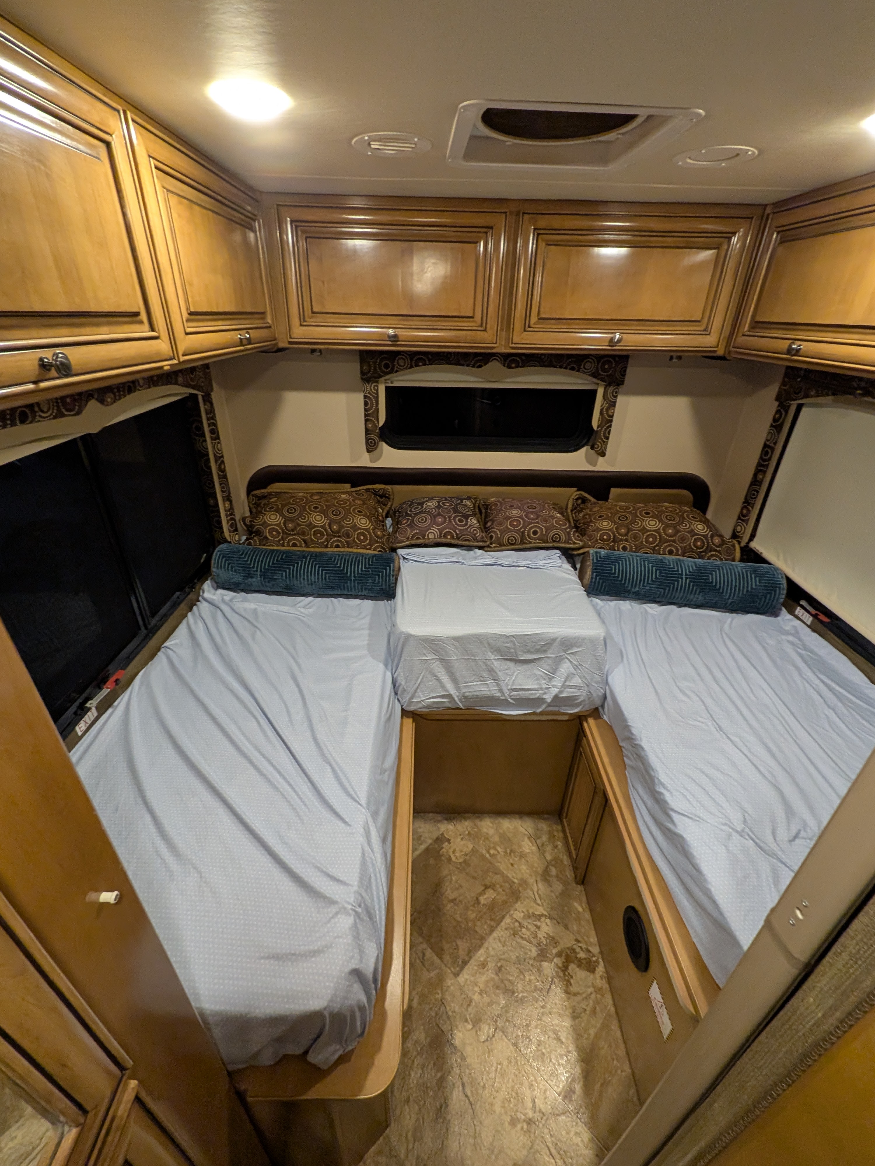 Inside a comfy **RV rental**: A bedroom with two beds, overhead cabinets, patterned pillows, and a connecting center platform.. Thor Siesta 2016