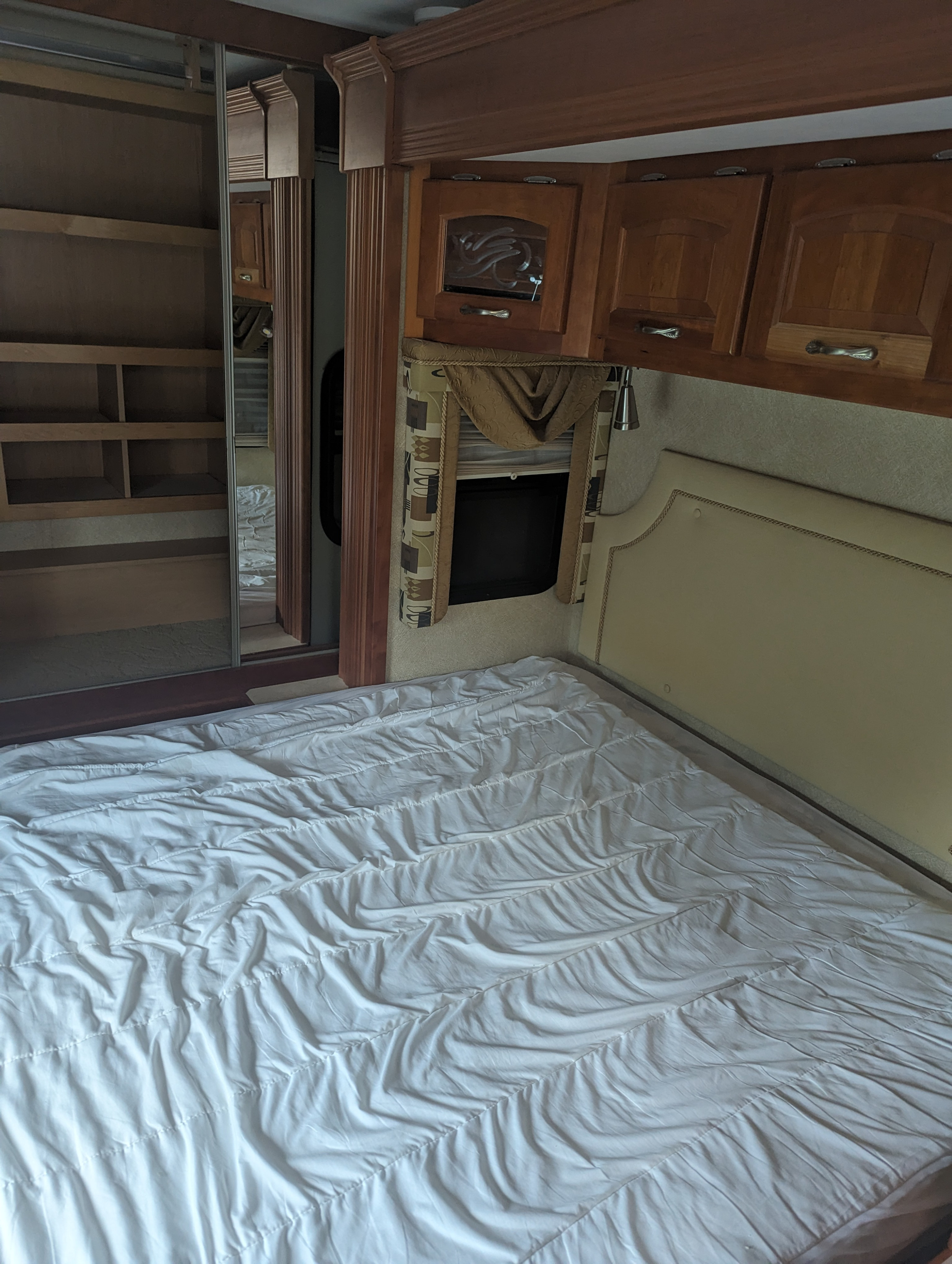 RV rental bedroom featuring a made bed, wood cabinets, a window with valance, and a mirrored wardrobe.. Kountry Star Kountry Star Motorhome 2008