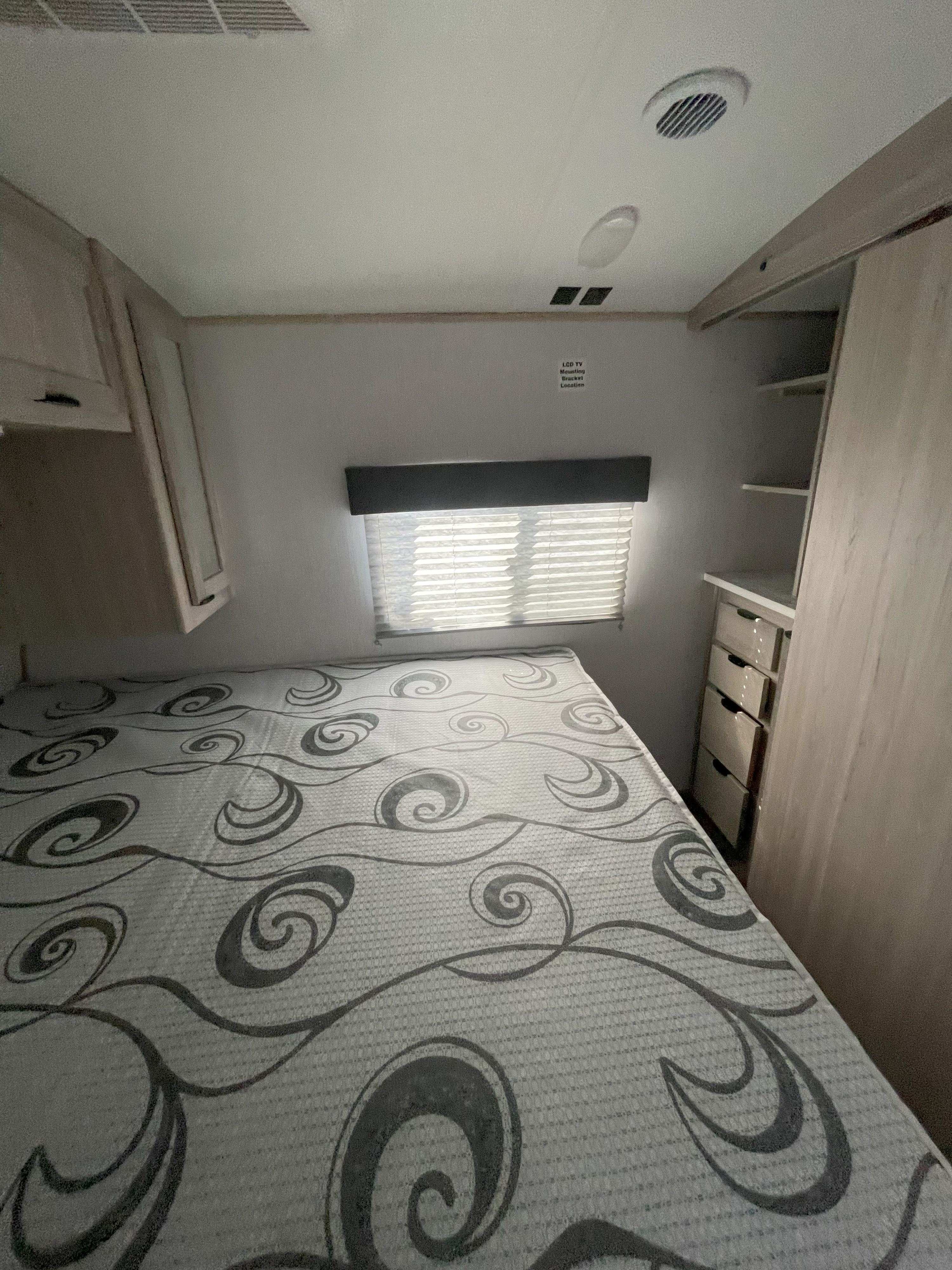 Cozy RV rental bedroom with patterned bed, overhead cabinets, window, and built-in storage. Ideal for comfortable travel.. Cruiser RV Shadow Cruiser 2023