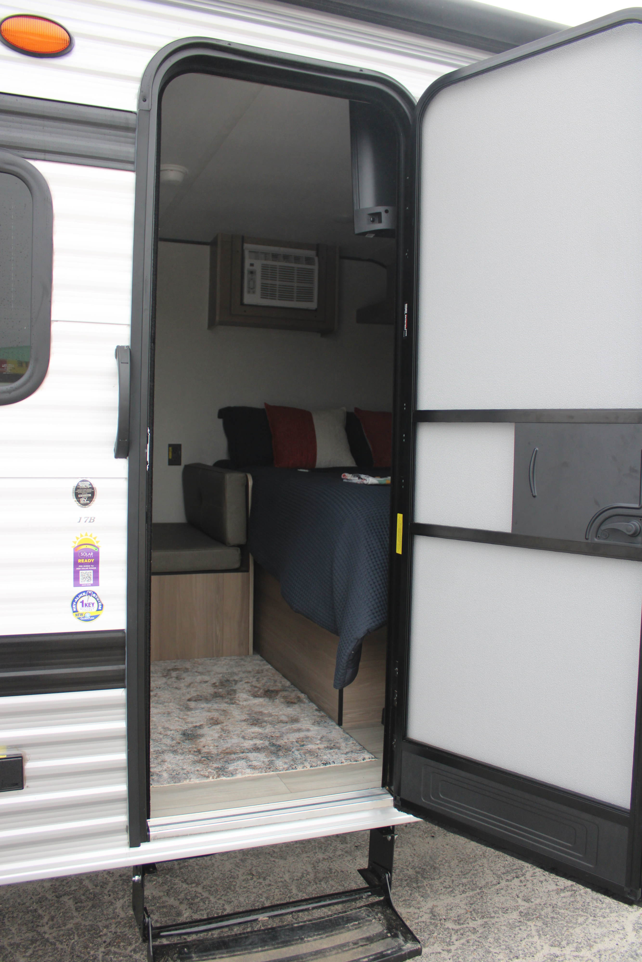 RV rental interior revealed: steps up to a cozy bed, seating, and mounted AC unit inside this travel trailer.. Keystone RV Coleman 17B 2025