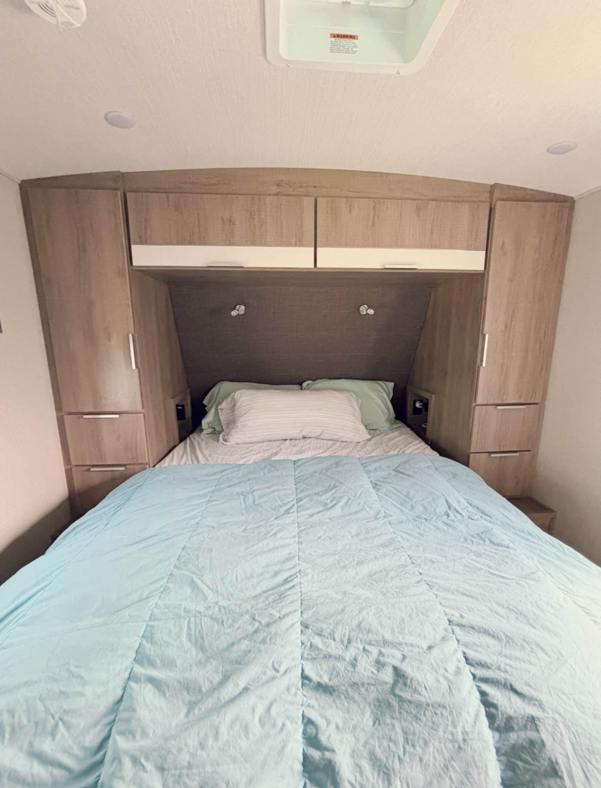 Comfortable RV rental bedroom with spacious bed, overhead cabinets, and wardrobe storage for a cozy travel experience.. Grand Design Imagine 2021