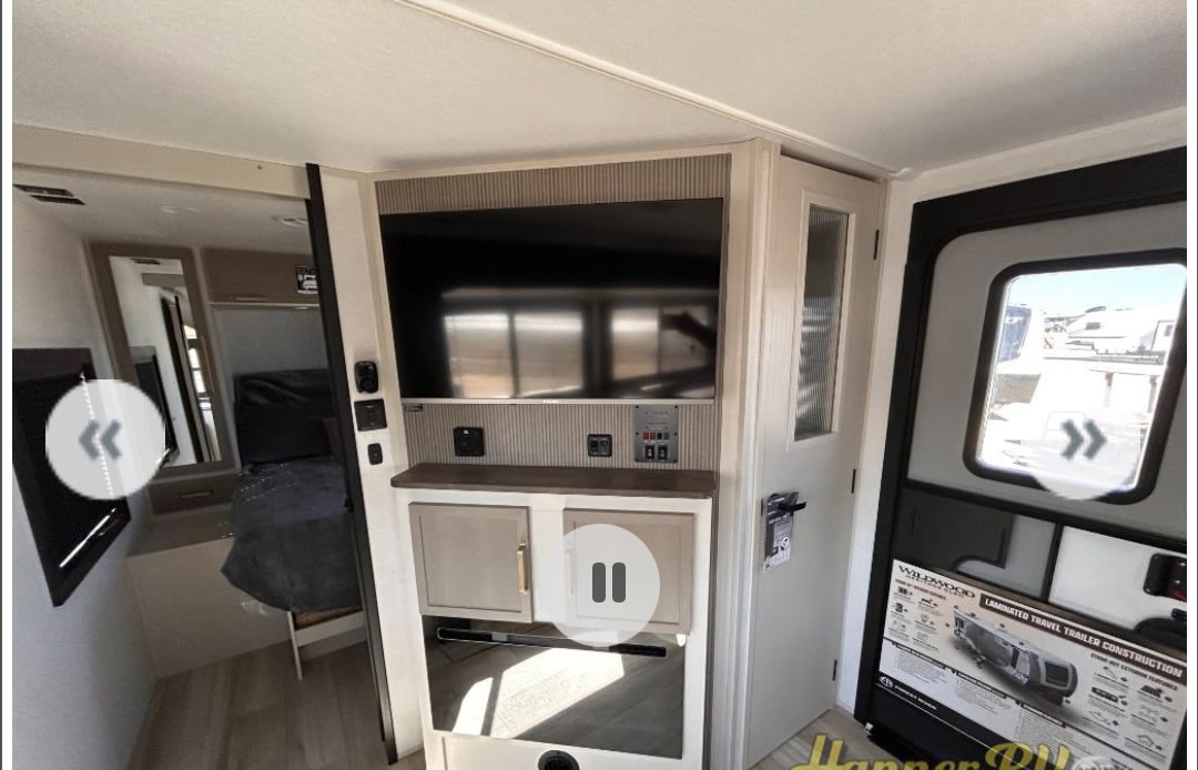 Inside a well-appointed RV rental: main living area with a large TV, control panel, cabinets, and adjacent bedroom/entry.. Forest river Heritage glen 2025