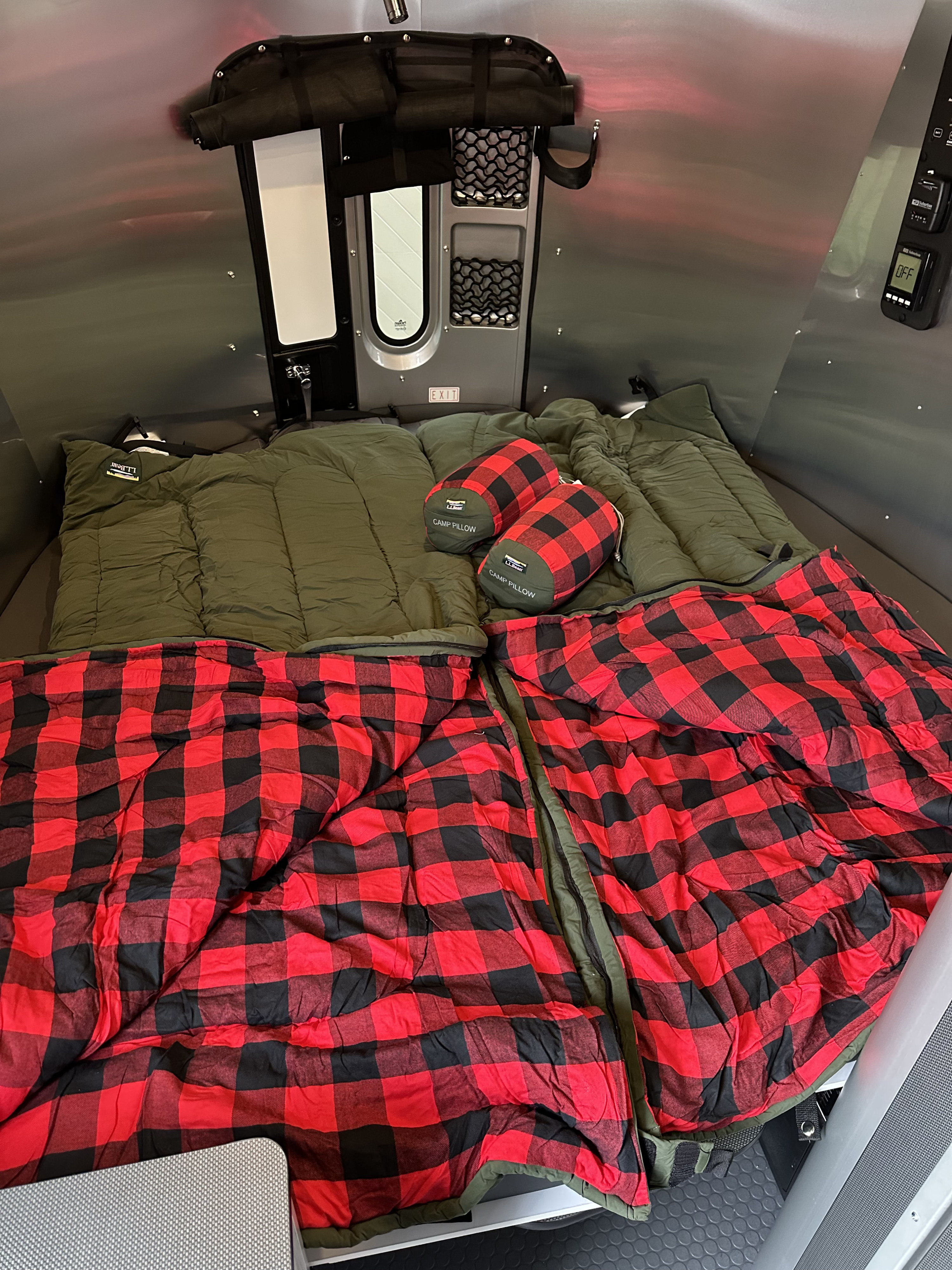 Inside a comfy RV rental: two olive green sleeping bags with red plaid blankets & L.L.Bean pillows. Ready for adventure!. Airstream Basecamp 2024