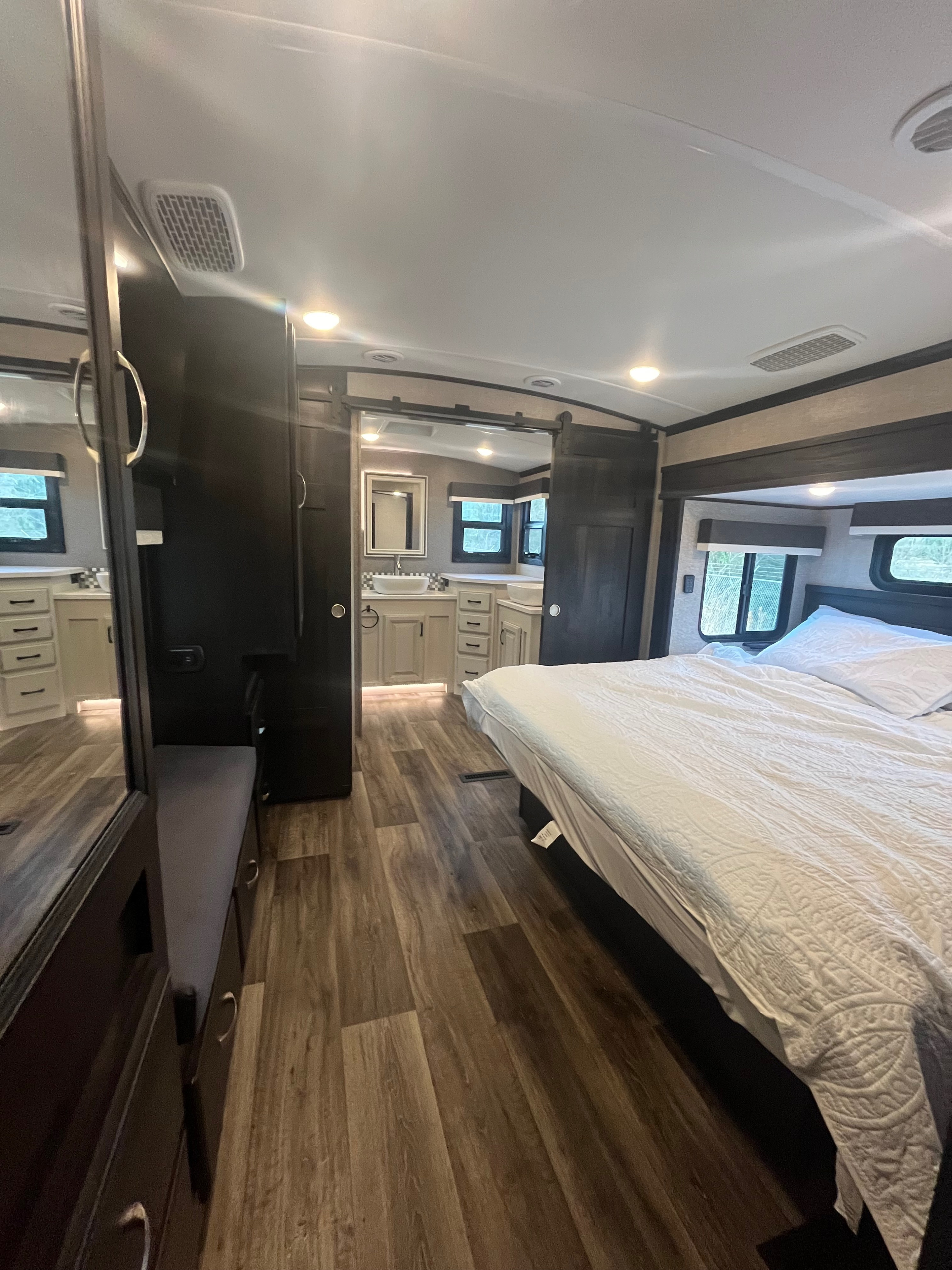 Modern RV rental bedroom featuring a large bed, wood-look flooring, and a private bathroom with dual sinks.. Jayco North Point 2022