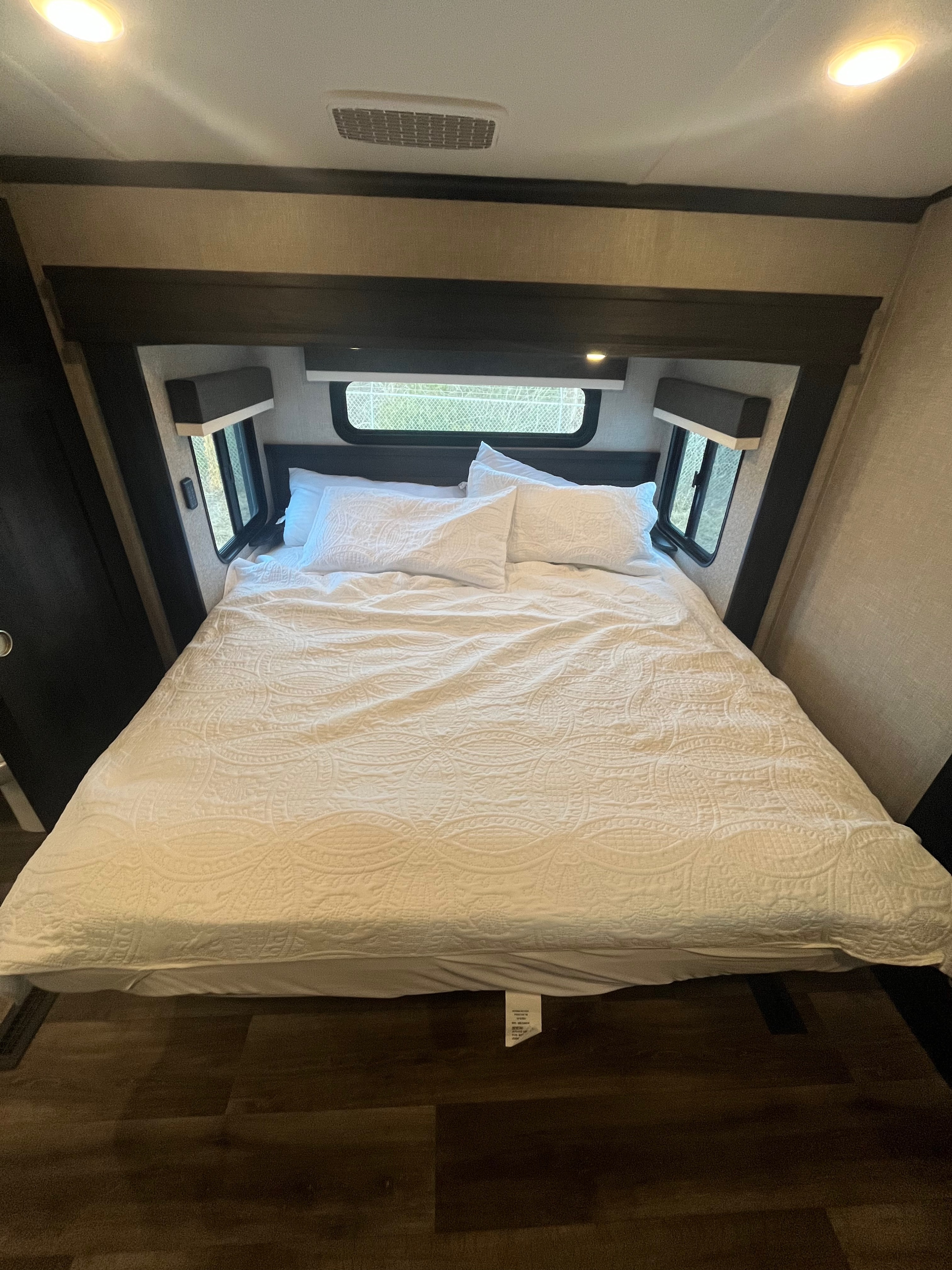 This RV rental features a cozy, well-lit bedroom with a neatly made bed, white patterned bedding, and exterior windows.. Jayco North Point 2022