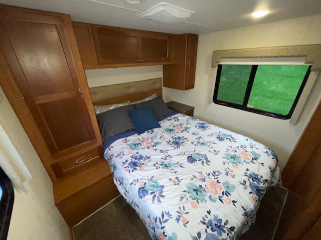 Comfortable RV rental bedroom: queen bed with floral comforter, wood cabinetry & window. Ideal for road trips.. Winnebago Spirit 2019