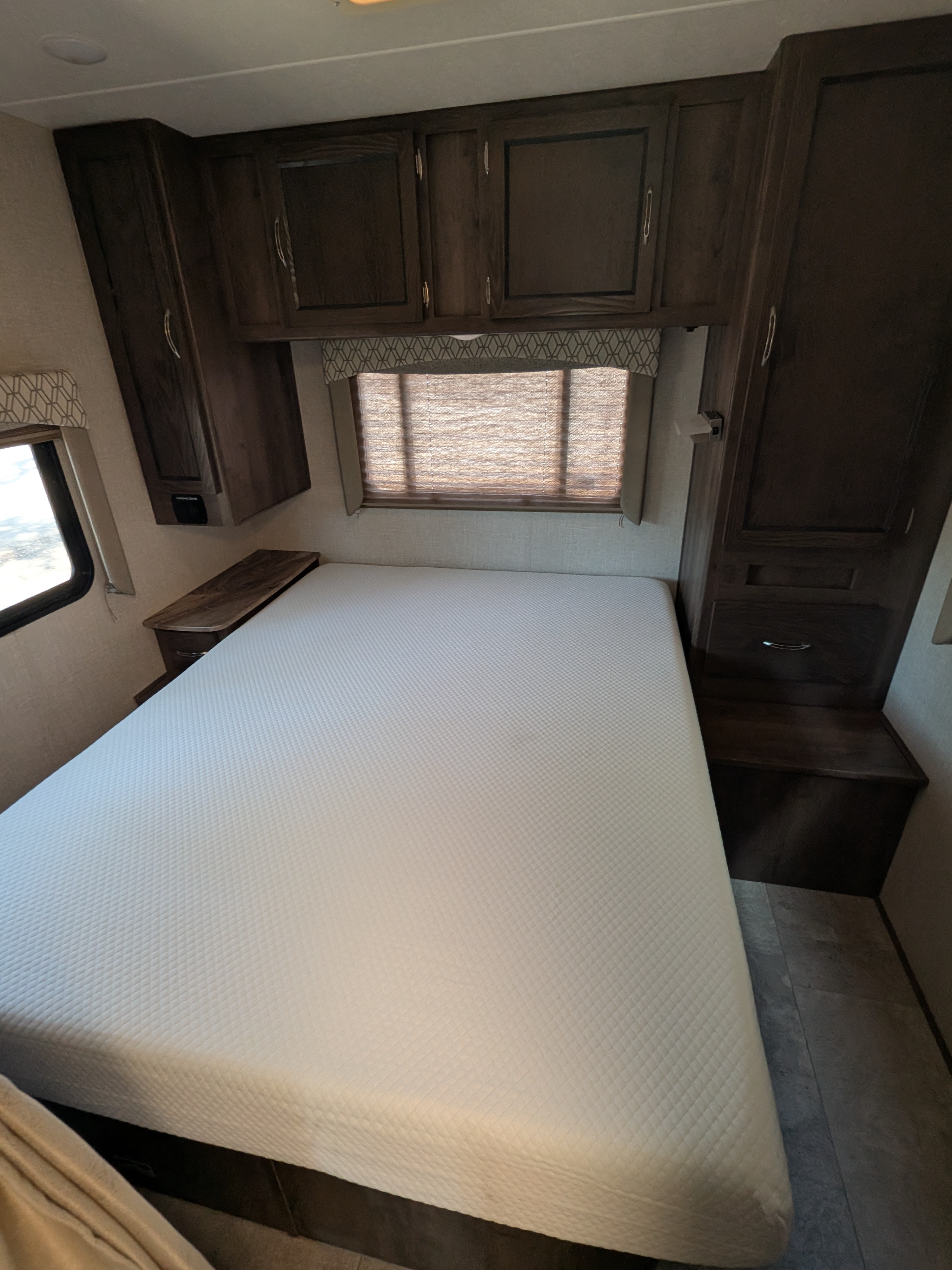RV rental bedroom with a white mattress, dark wood cabinets, and window, offering a comfortable travel stay.. Coachmen Freelander 2018