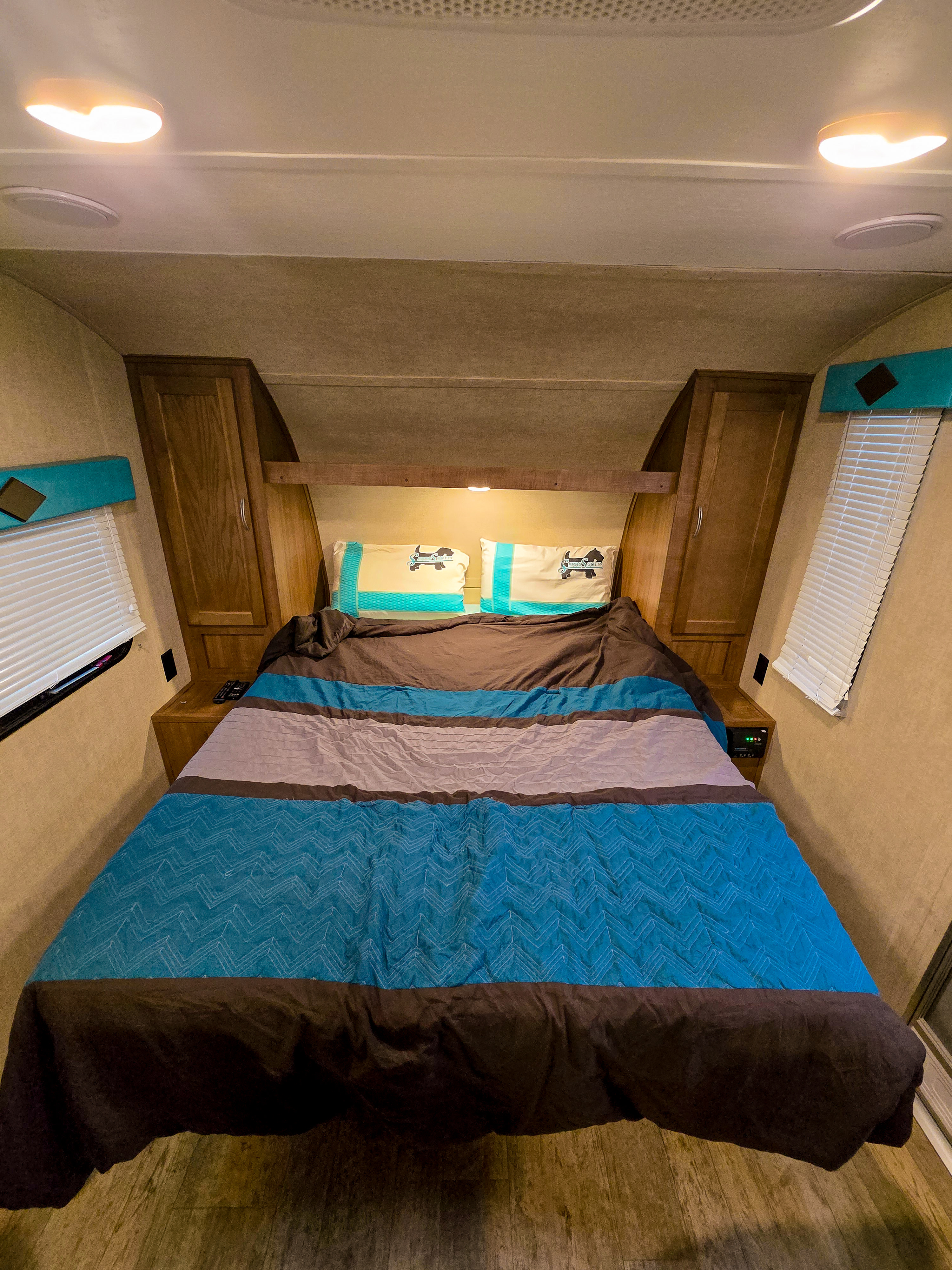 This RV rental interior shows a cozy bedroom with a large bed, brown and teal bedding, dog pillows, and wooden cabinets.. Gulf Stream SerroScotty 2017