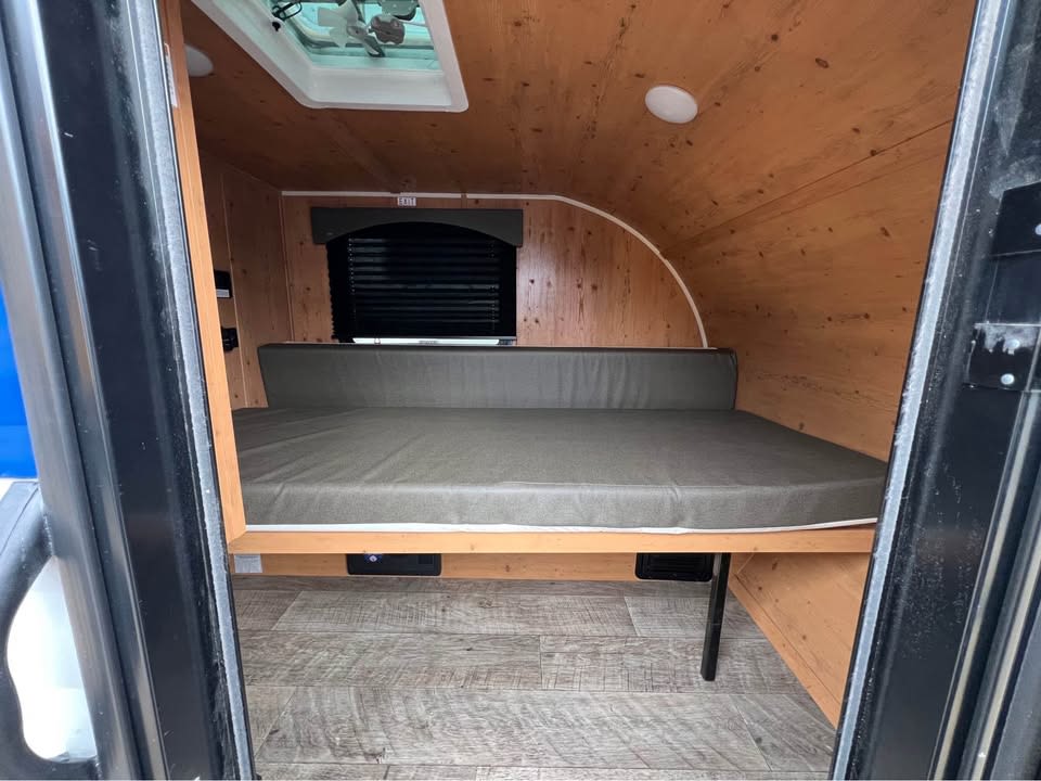 Compact RV rental interior featuring a wood-paneled, curved ceiling, a comfortable bed, and a skylight.. Sunset Park RV SunRay 2023