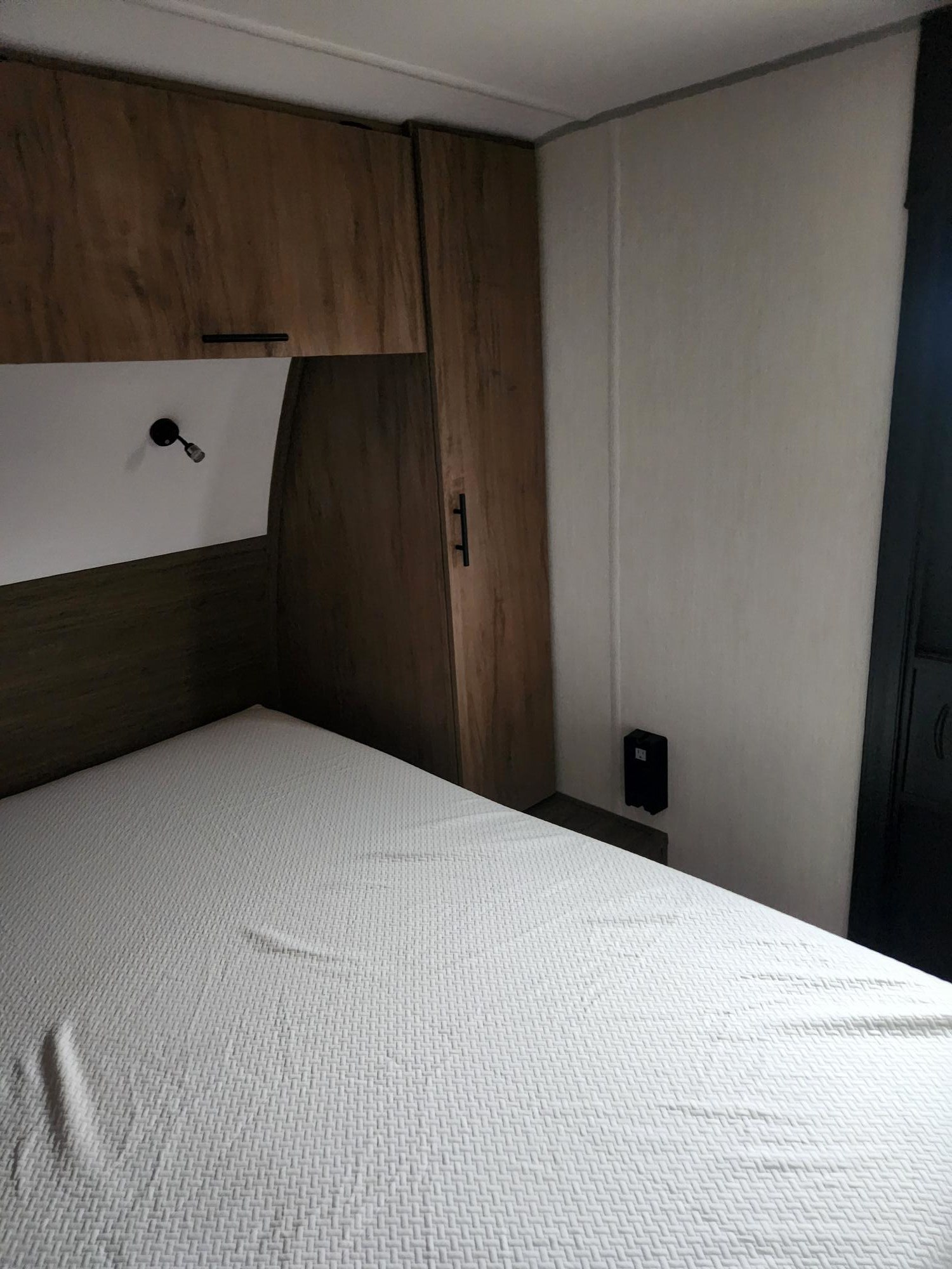 Bedroom in an RV rental featuring a white bed, wood cabinets, and a reading light. A functional, compact space.. Forest River/ Grey Wolfe Black Label 29NMBL 2025