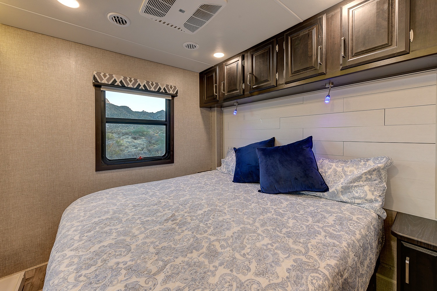 RV rental bedroom: Cozy bed, dark wood cabinets, and a beautiful desert window view for your travel adventure.. Entegra Coach Vision XL 2023