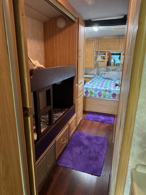 Cozy RV interior: bunk beds on left, wood-floored hallway with purple mats, main bedroom ahead. Ideal for an rv rental.. Fleetwood 39/MH 2000