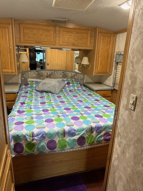 Cozy RV rental bedroom with colorful bedding, wooden cabinets, built-in storage, and mirror accents.. Fleetwood 39/MH 2000