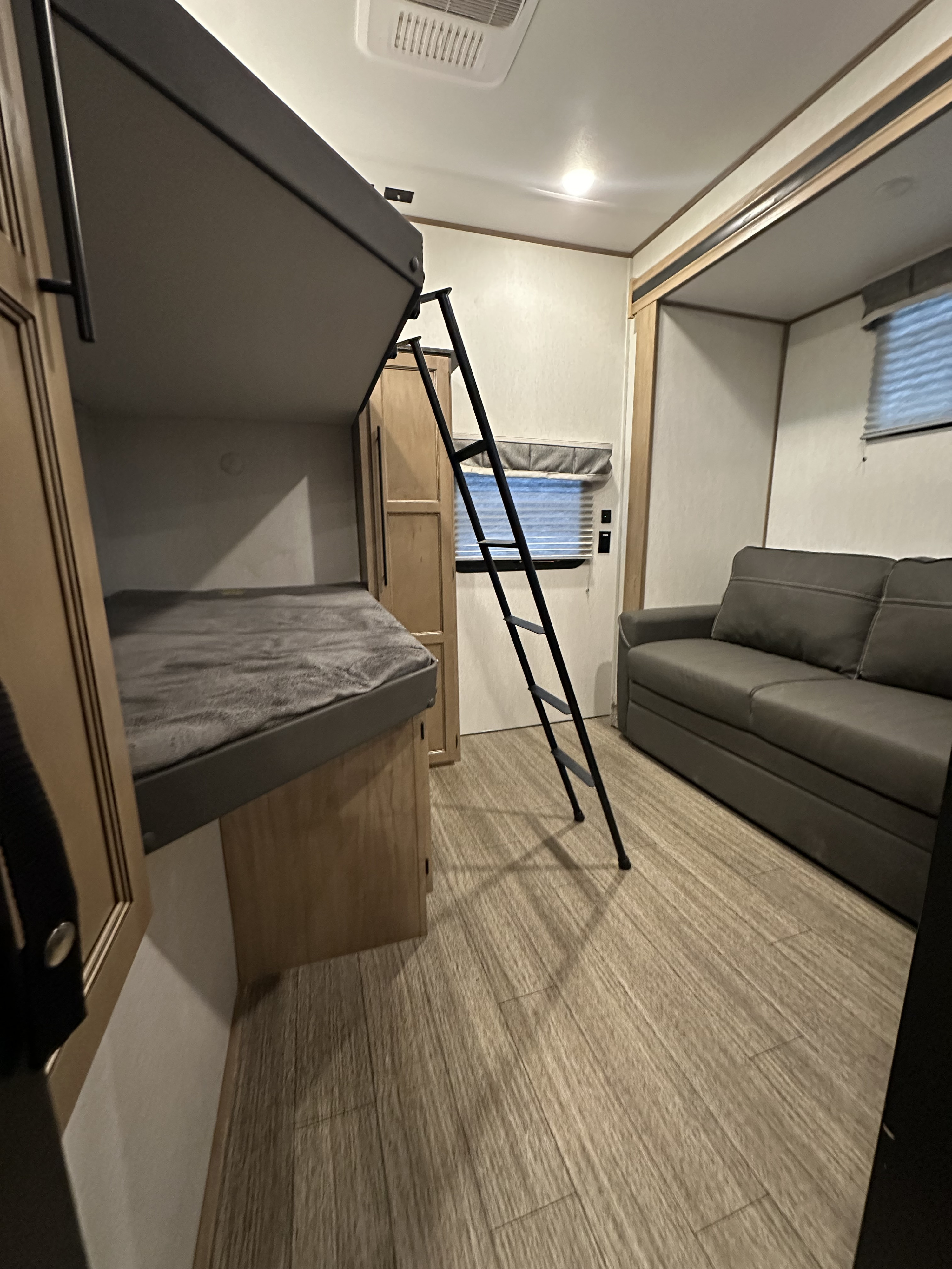 Inside an RV rental: a bunk bed with ladder, nearby sofa, cabinet, and light wood-look flooring create a functional space.. Forest River Sabre 2023