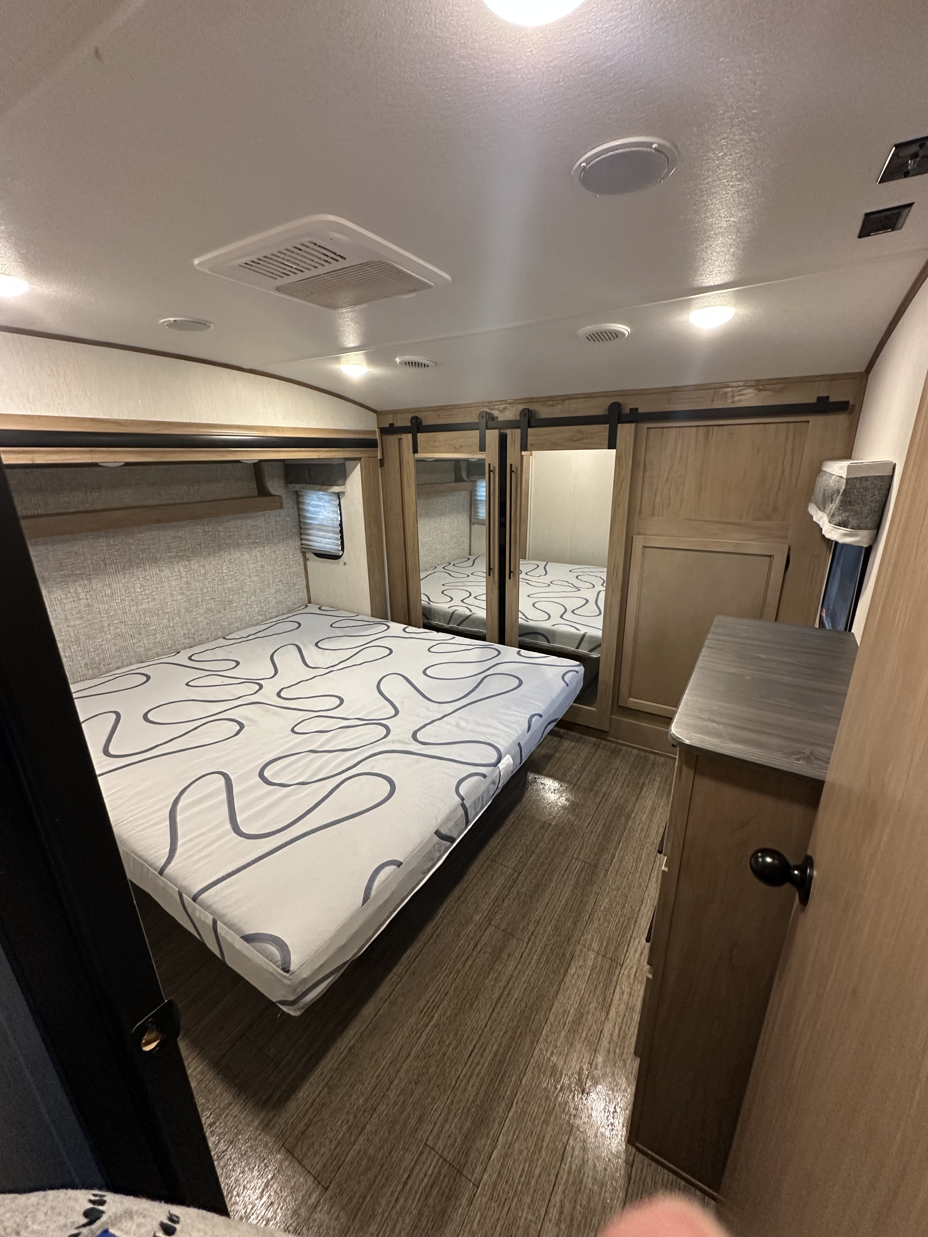 RV rental bedroom showcasing a bed with unique wavy pattern, mirrored closet doors, and wood-look flooring.. Forest River Sabre 2023