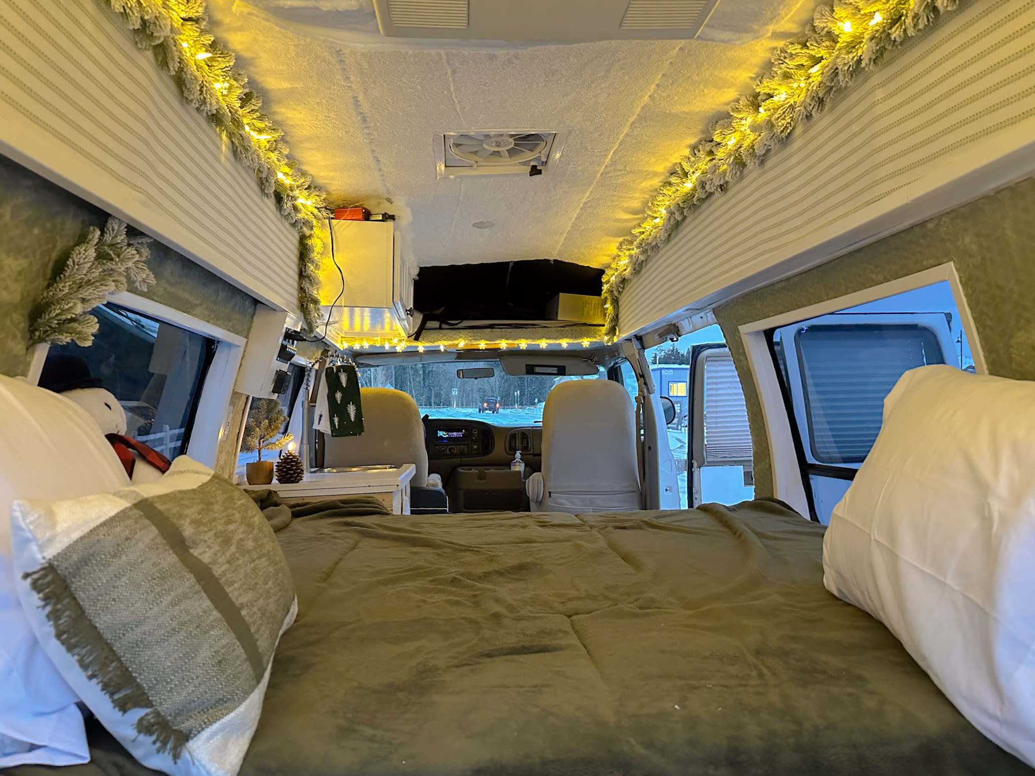 Cozy RV rental interior: festive lights, frosted garland, and a comfy bed. View towards the driver's cabin.. Jayco Conversion Van 1998