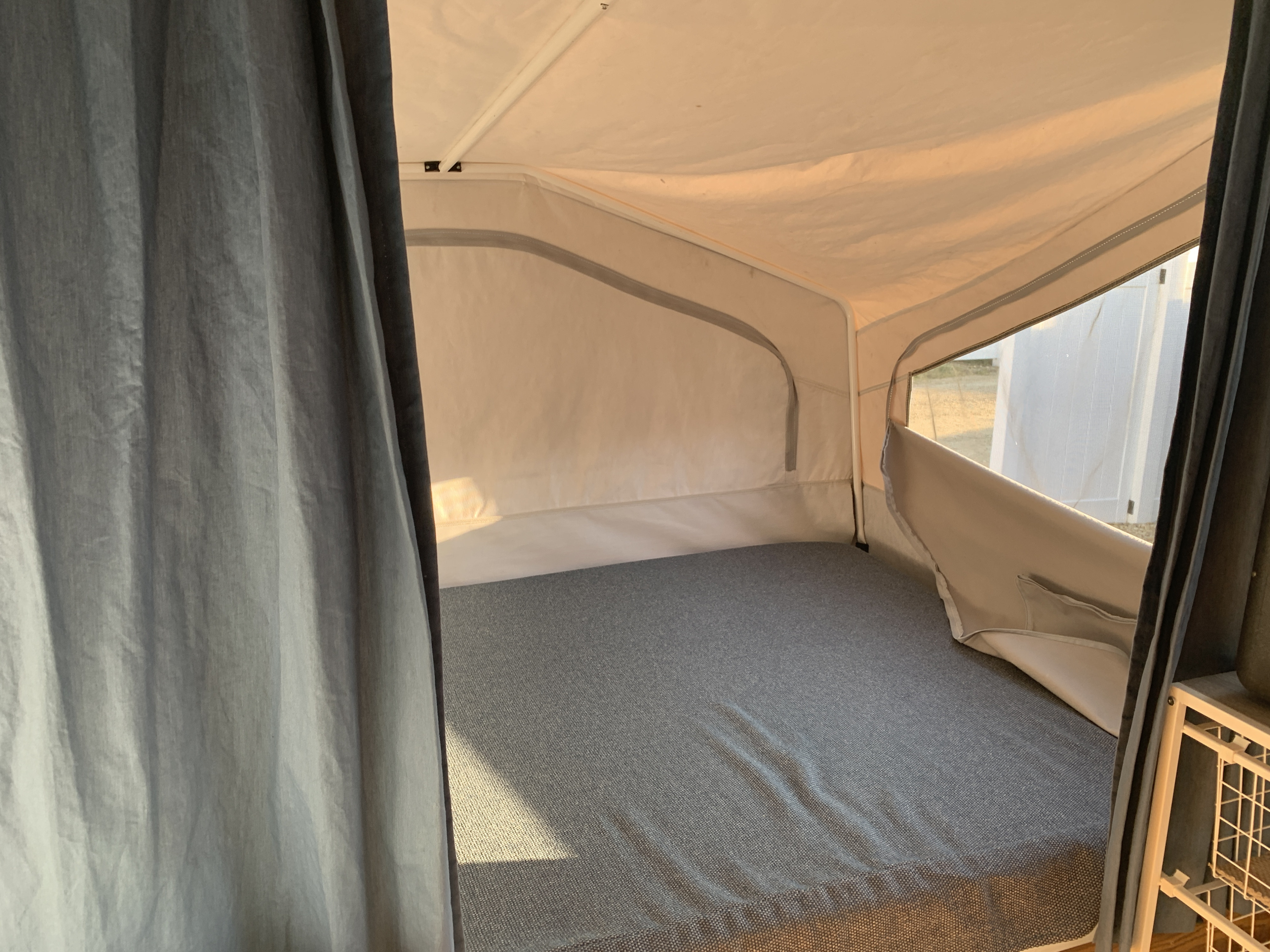 Inside an RV rental: a comfy pop-up camper bed with grey sheets, soft canvas walls, and sunny window view.. Forest River Flagstaff 2000