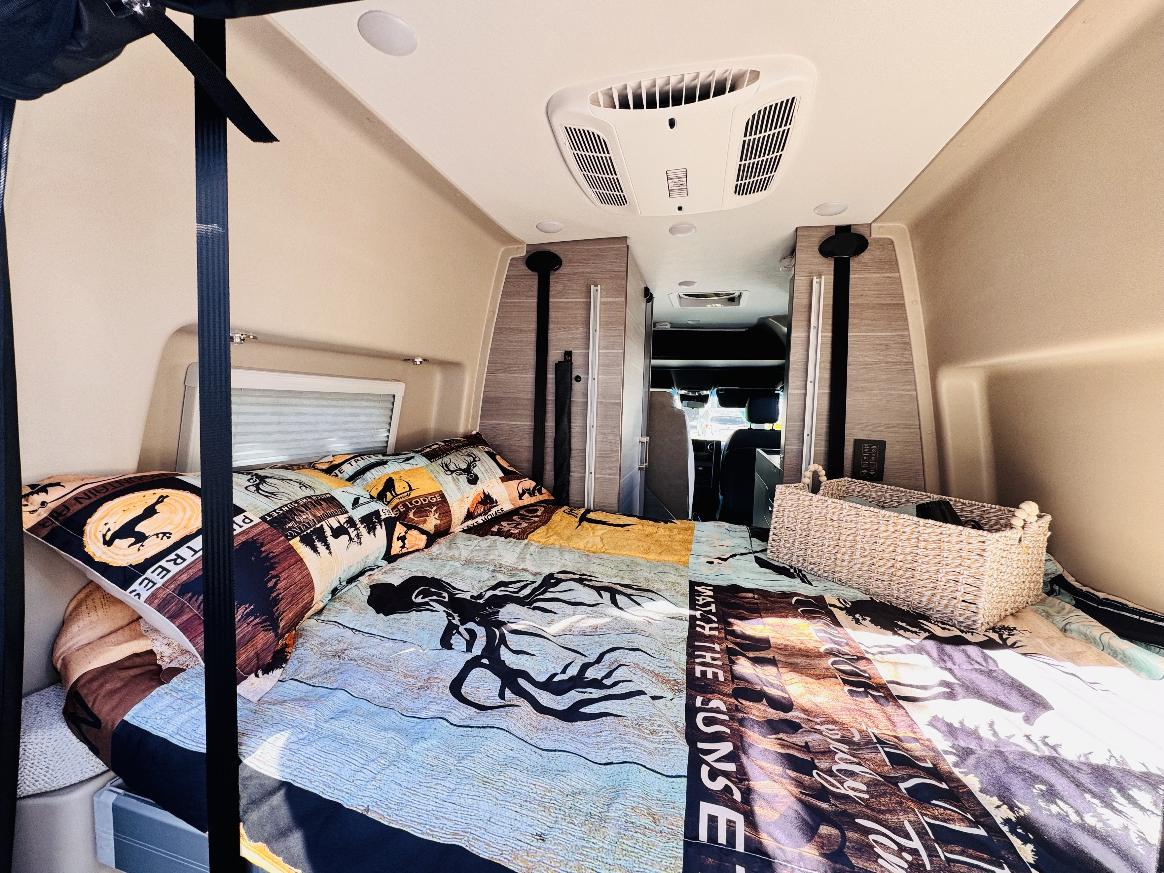 Cozy RV rental bed with nature-themed bedding, overhead AC, and storage basket. Ready for your next adventure.. Entegra Coach Launch 2024