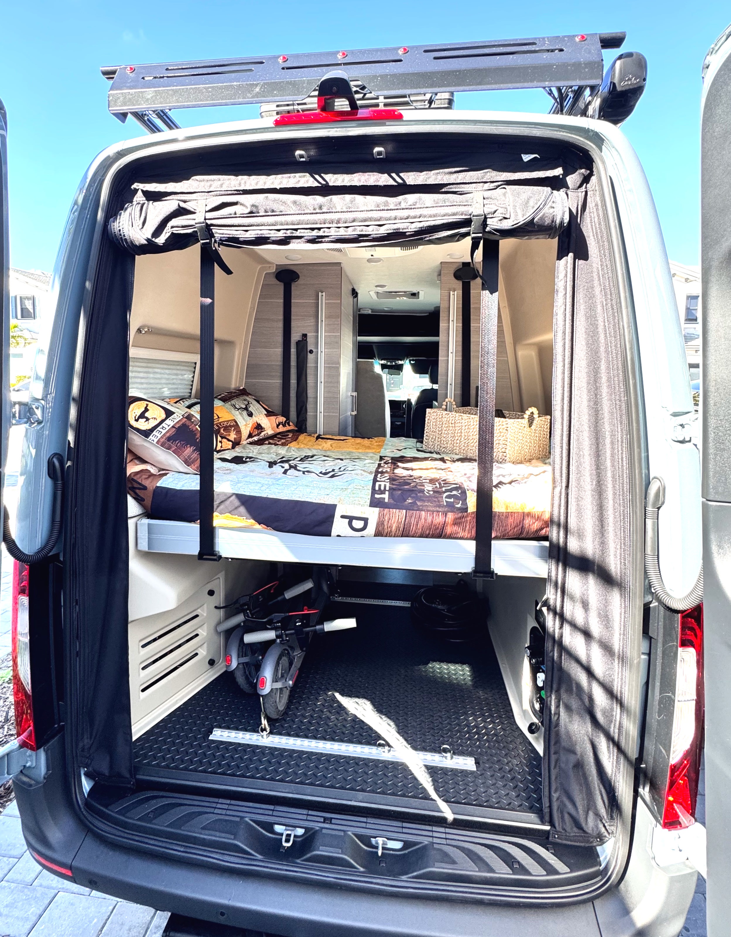 Inside an RV rental: a cozy bed above spacious storage with scooters, visible from the open rear doors.. Entegra Coach Launch 2024