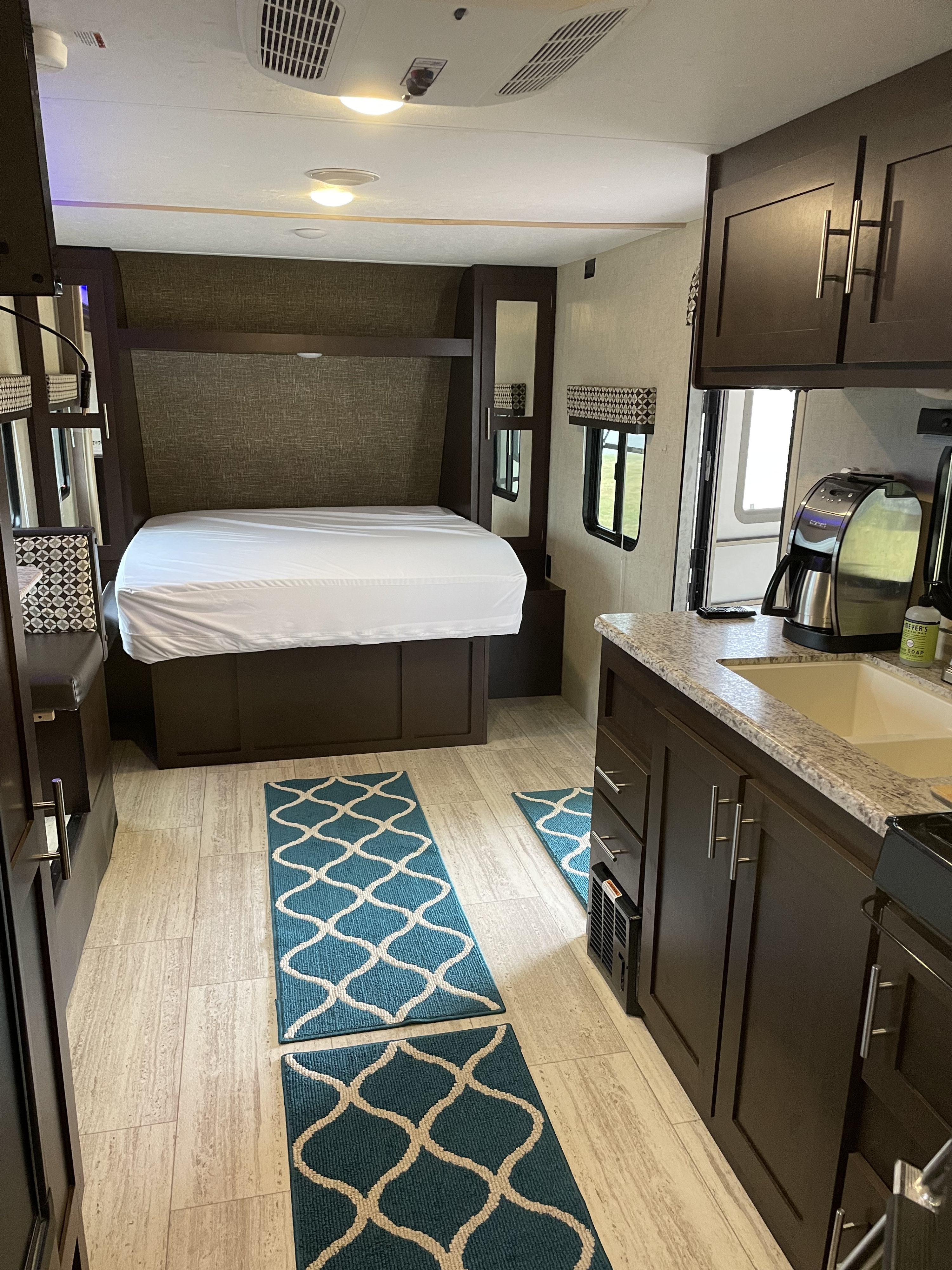 Experience a modern RV rental interior featuring a cozy bedroom, bright blue geometric rugs, and a compact kitchen setup.. Sportsmen Sportsmen Trailer 2017