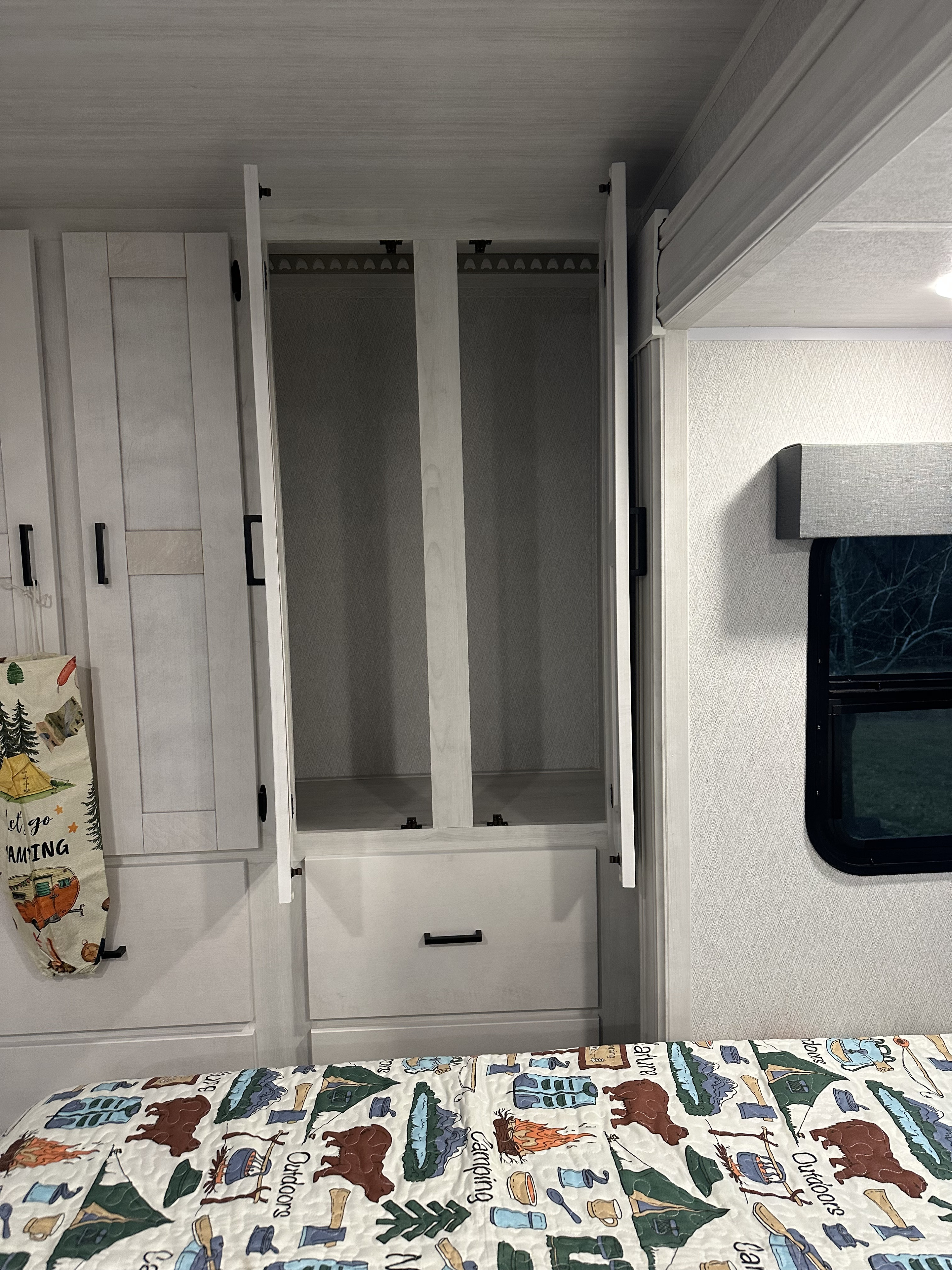 RV rental bedroom interior featuring an open light-wood closet, drawer, and a bed with camping-themed quilt and decor.. East to West Entrada 24FM 2024