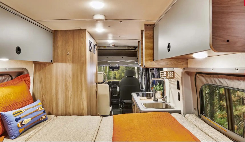 Cozy rv rental interior featuring a comfortable bed with colorful pillows, kitchenette, and scenic forest views for your travels.. Winnebago Solis NPF 2025