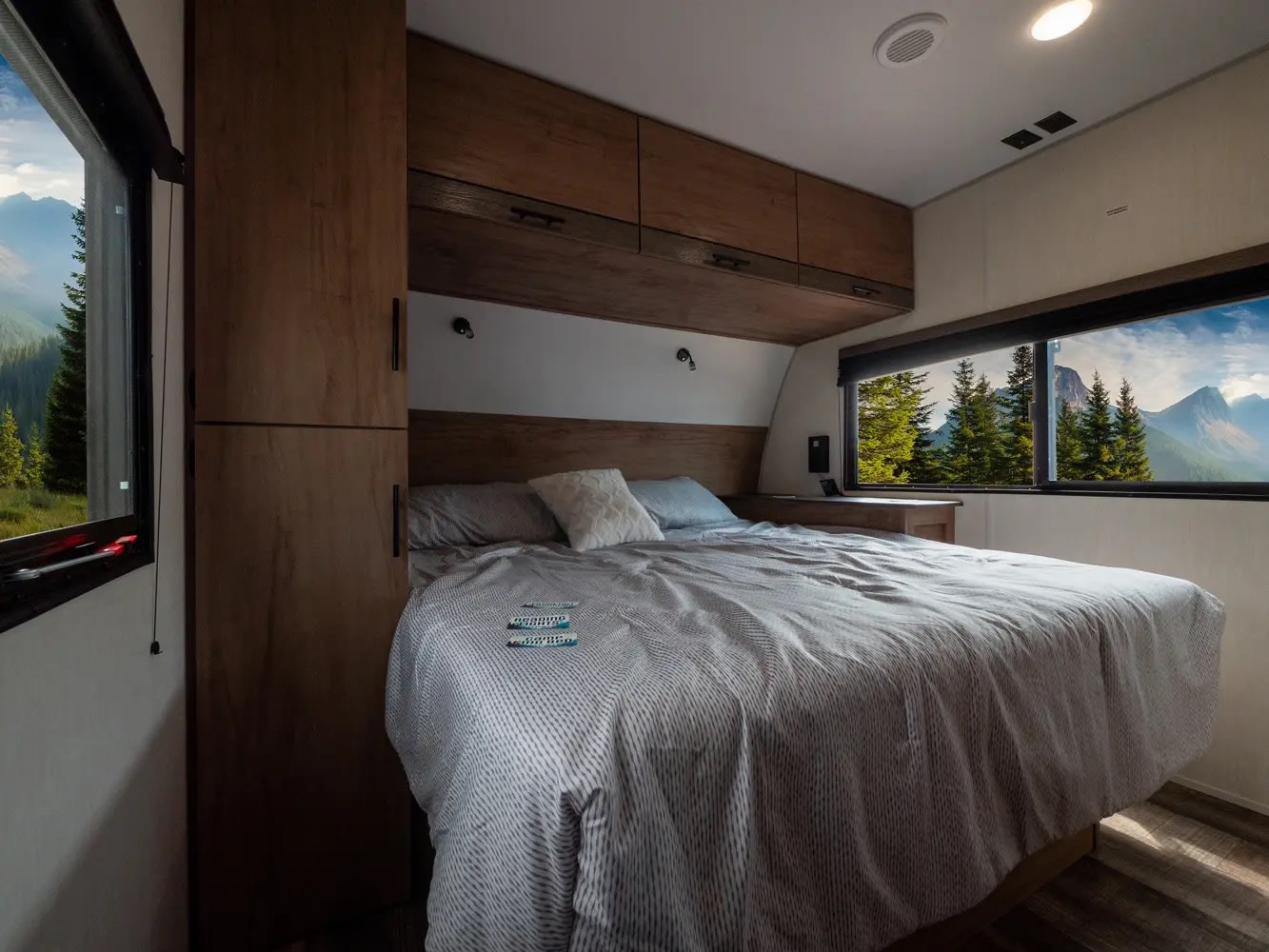Experience comfort in this RV rental bedroom featuring a striped bed, wooden cabinetry, and breathtaking mountain views from large windows.. Forest River Campsite Reserve 2025