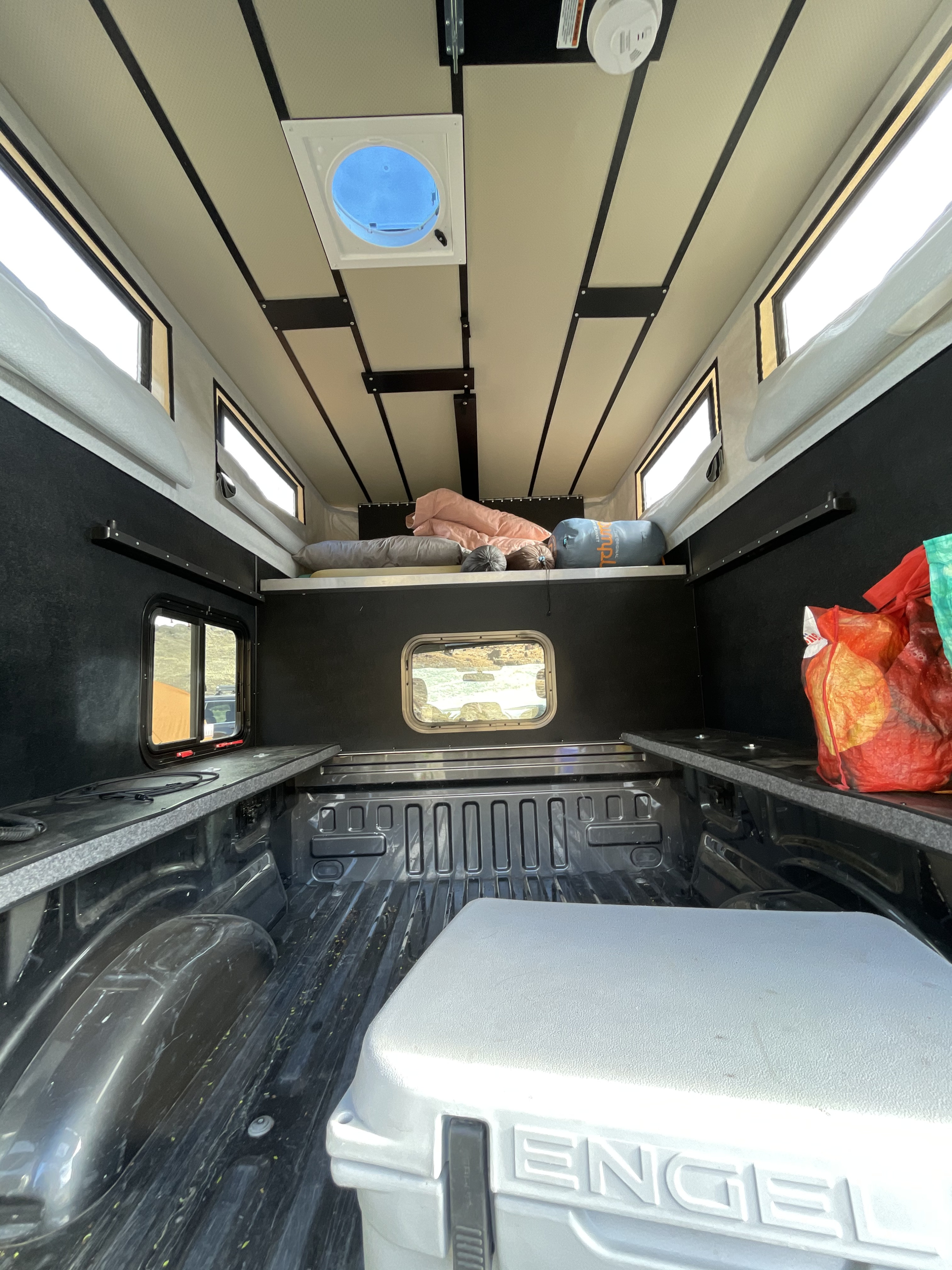 Inside an RV rental truck bed camper: A cozy sleeping platform, side storage, Engel cooler, windows, and roof vent are visible.. Four Wheel Campers Shell Models 2020