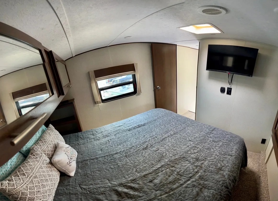 RV rental bedroom with a large bed, decorative pillows, window, and wall-mounted TV. Great for travel!. Forest River Impression 2018