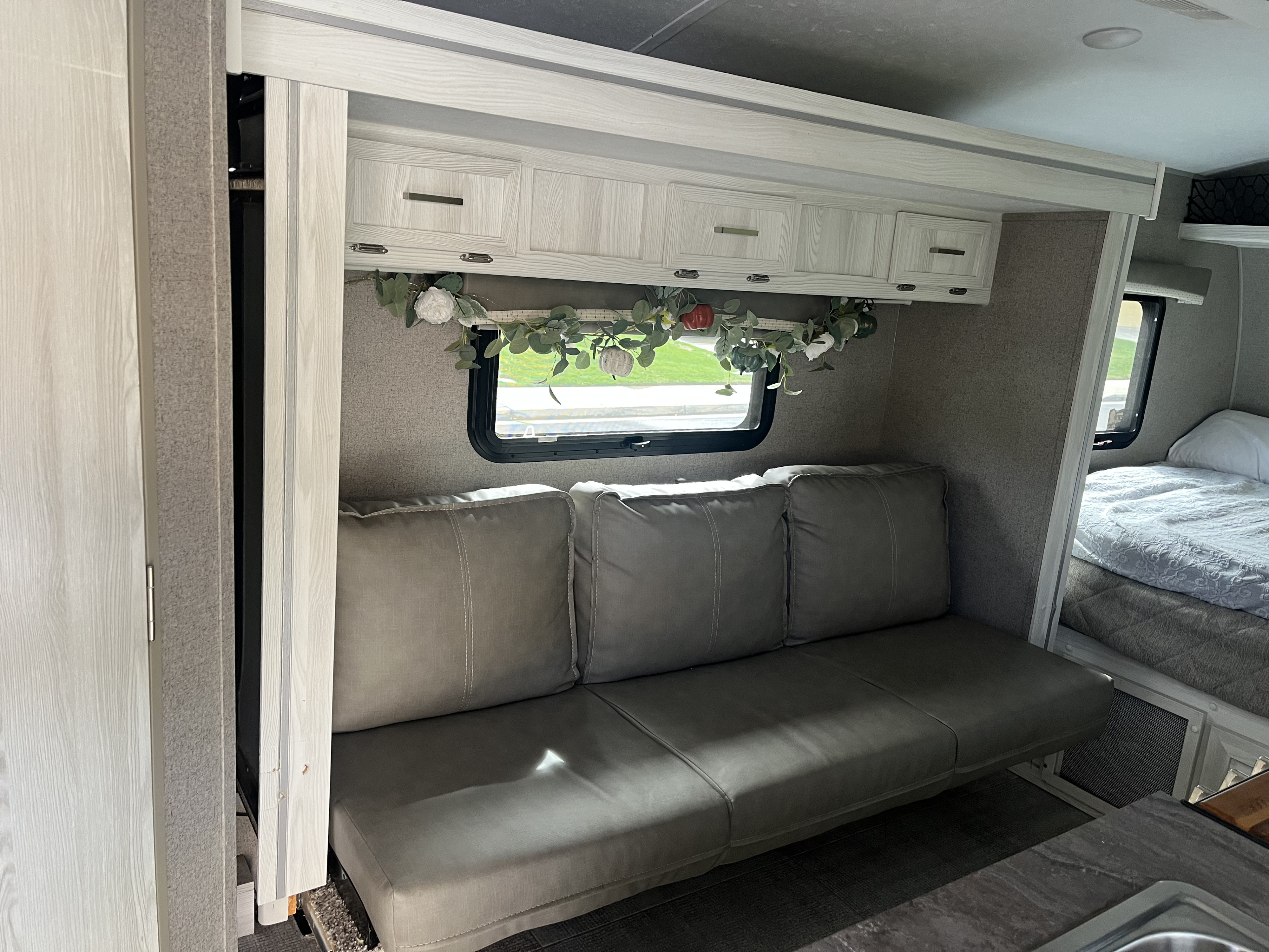 Inside a modern RV rental: Comfortable gray sofa, light wood cabinets, and fall-themed window garland, with a bed visible.. Forest River Rockwood Geo Pro 2021