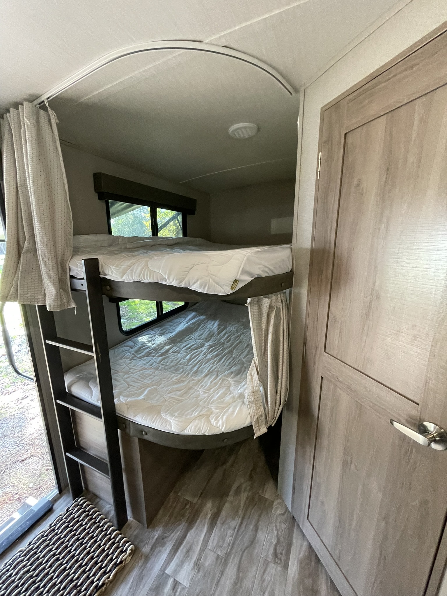 View inside an RV rental, showing two comfortable bunk beds with windows and a ladder, next to a wood-look interior door.. Grand Design Imagine 2021