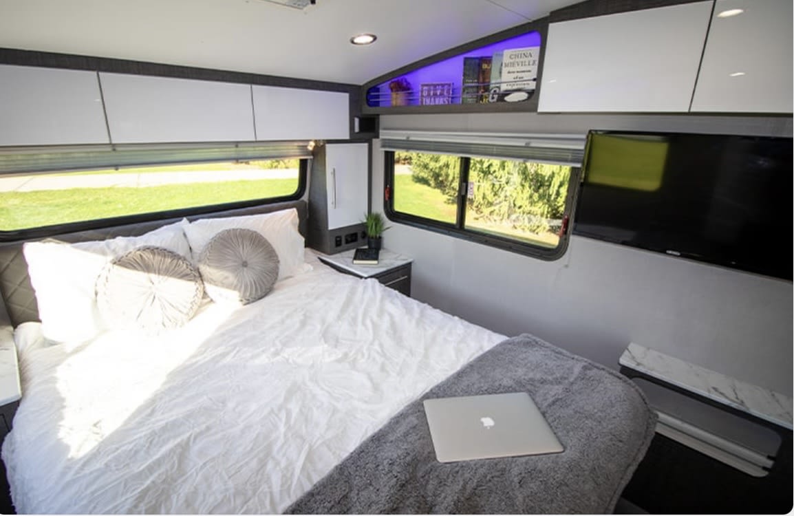 Spacious and modern RV rental bedroom with a comfortable bed, overhead cabinets, a TV, and scenic views, ideal for travel.. InTech RV InTech RV Trailer 2023