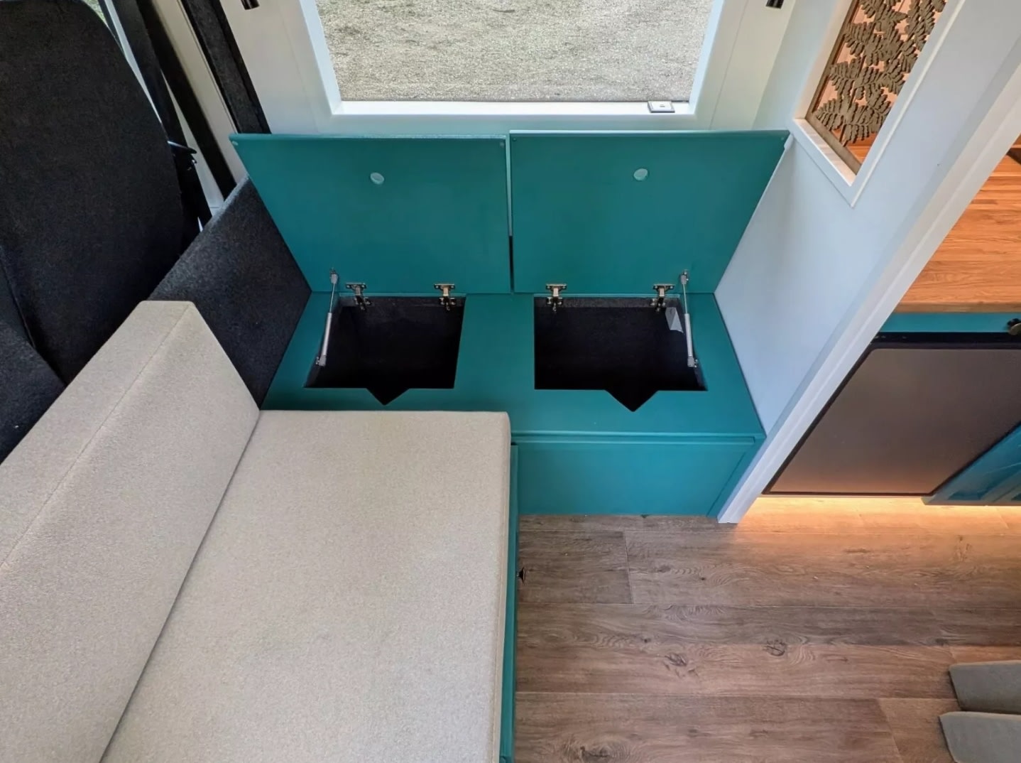 Inside an RV rental: The interior shows two open teal storage compartments with lift-up lids next to a light-colored sofa.. Peugeot Boxer L4H2 2021