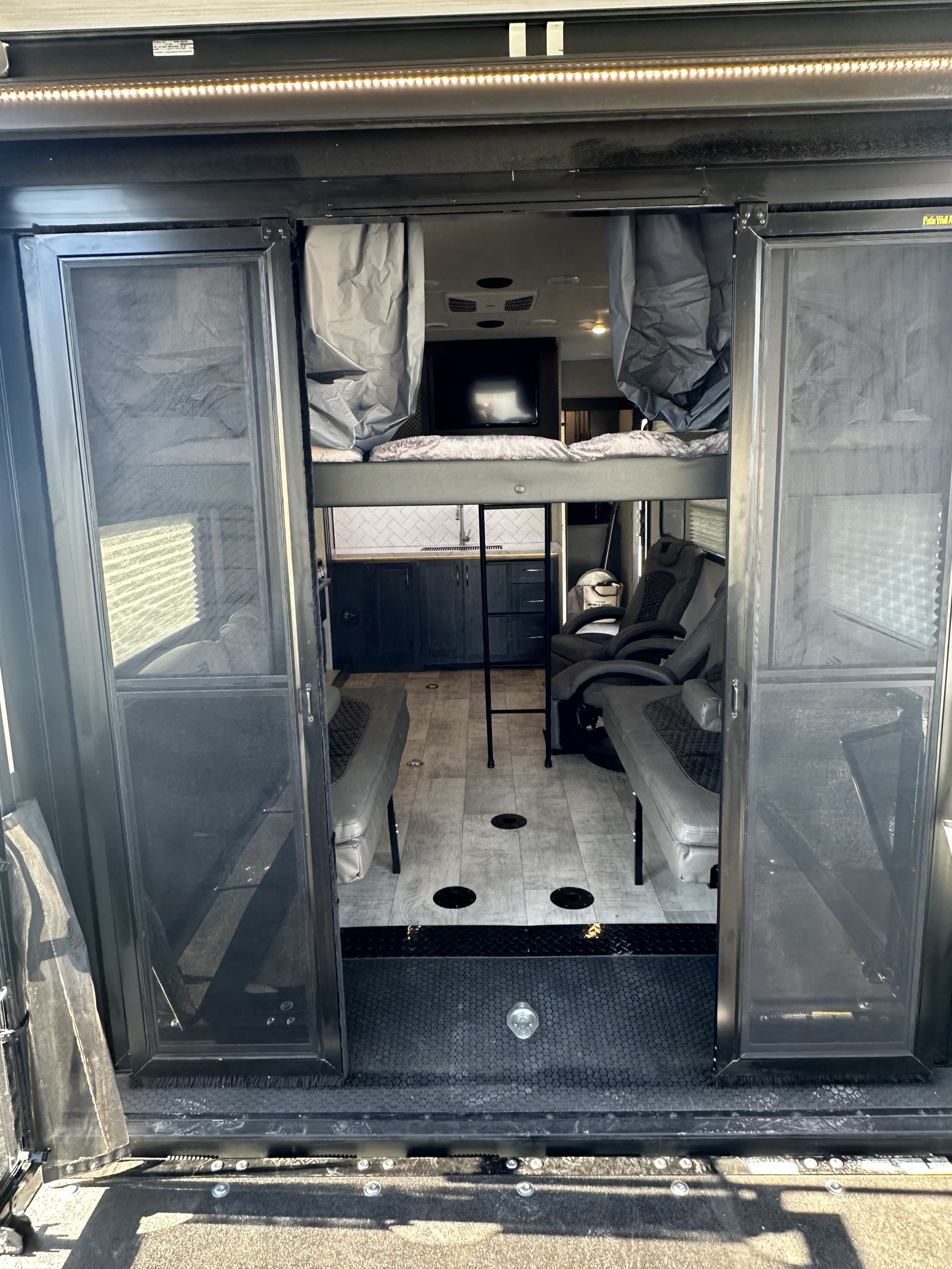 Interior view of an rv rental, showcasing a bunk bed, kitchenette, seating, and durable flooring, seen from the open ramp.. Grand Design Momentum 2022