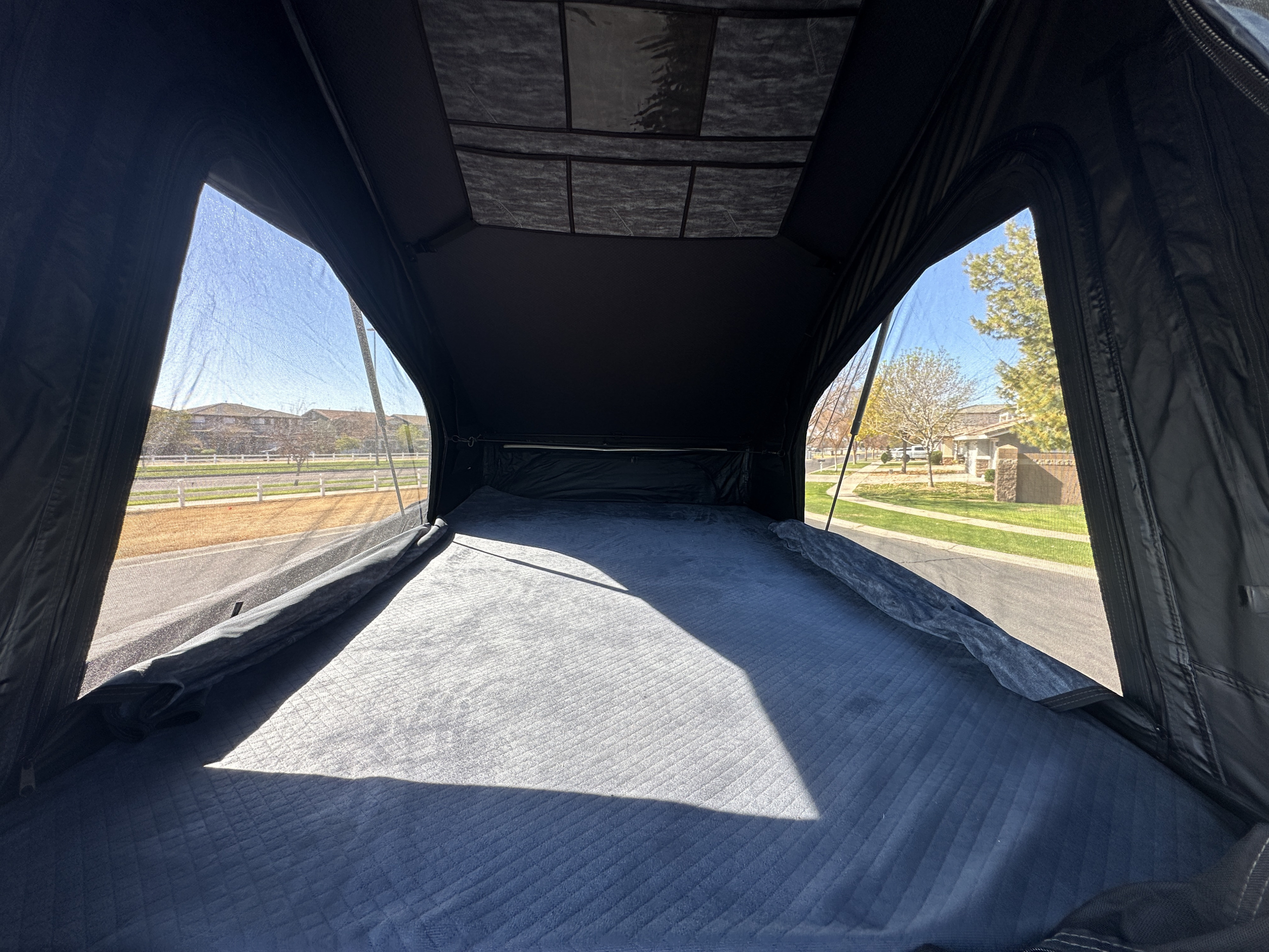 Inside a comfortable rooftop tent, perfect for an RV rental adventure. Features a cozy bed and mesh windows with outdoor views.. Jeep Overlander 2019