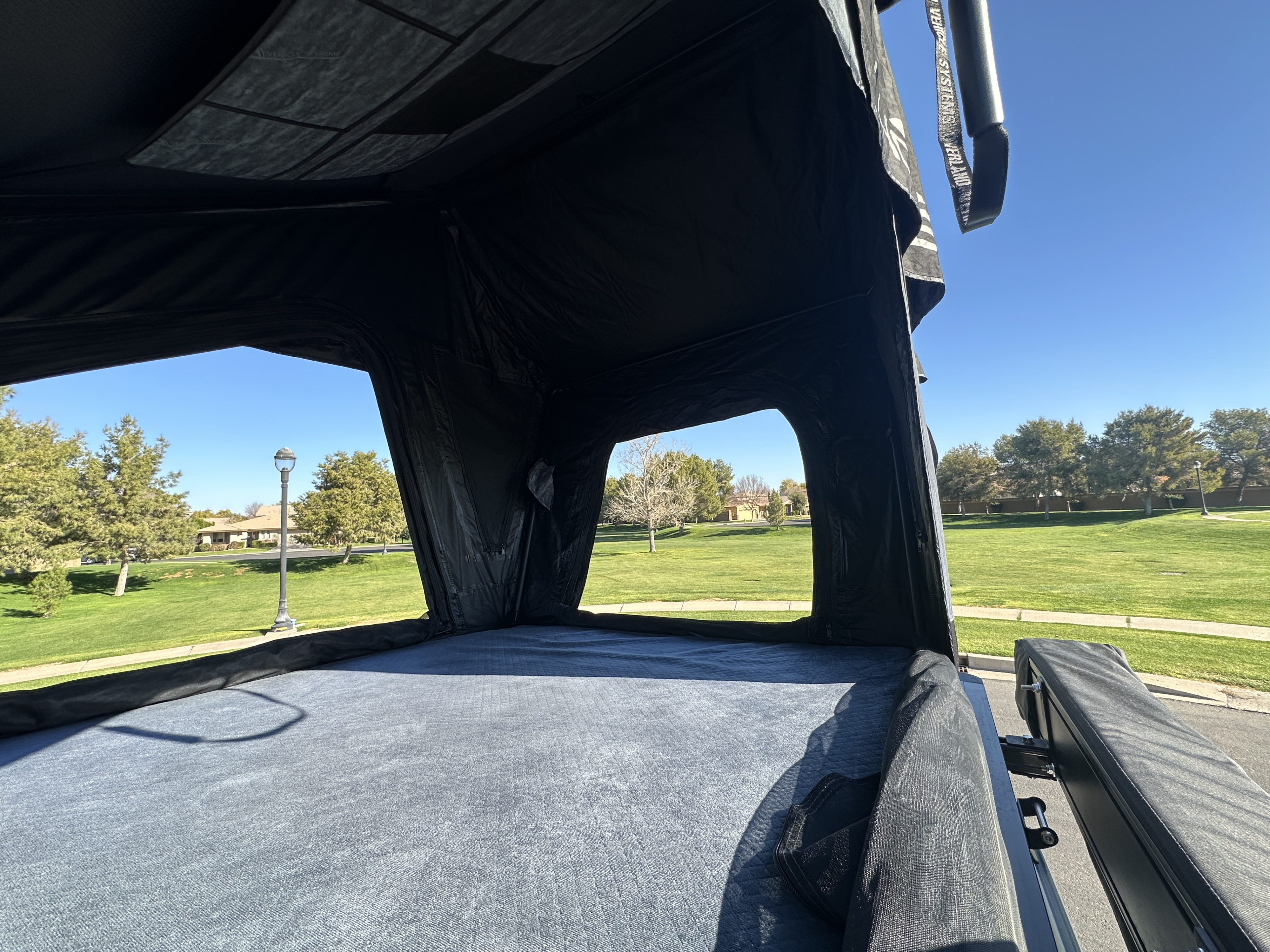 RV rental rooftop tent interior: a cozy grey mattress and open windows revealing a sunny park view. Perfect for camping.. Jeep Overlander 2019