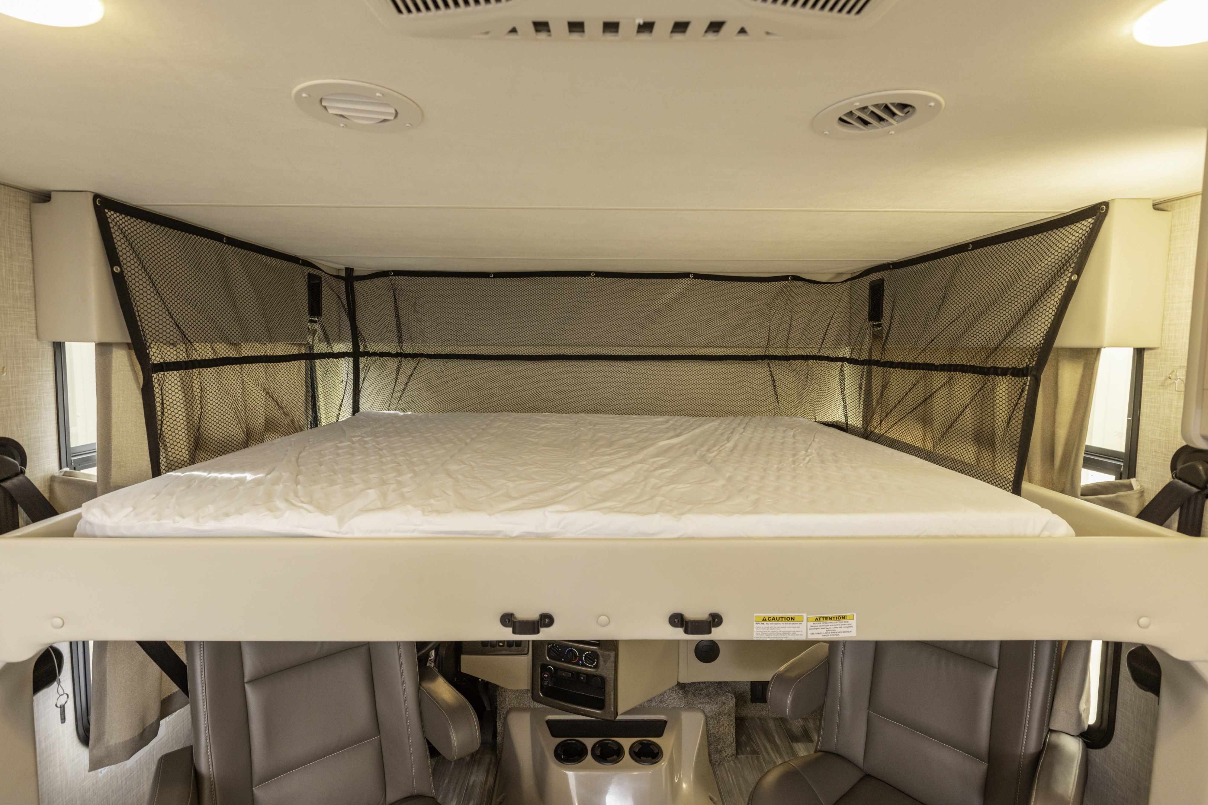Cozy cab-over bunk in RV rental, with safety net, positioned above vehicle controls and seating area.. Thor Hurricane 2023