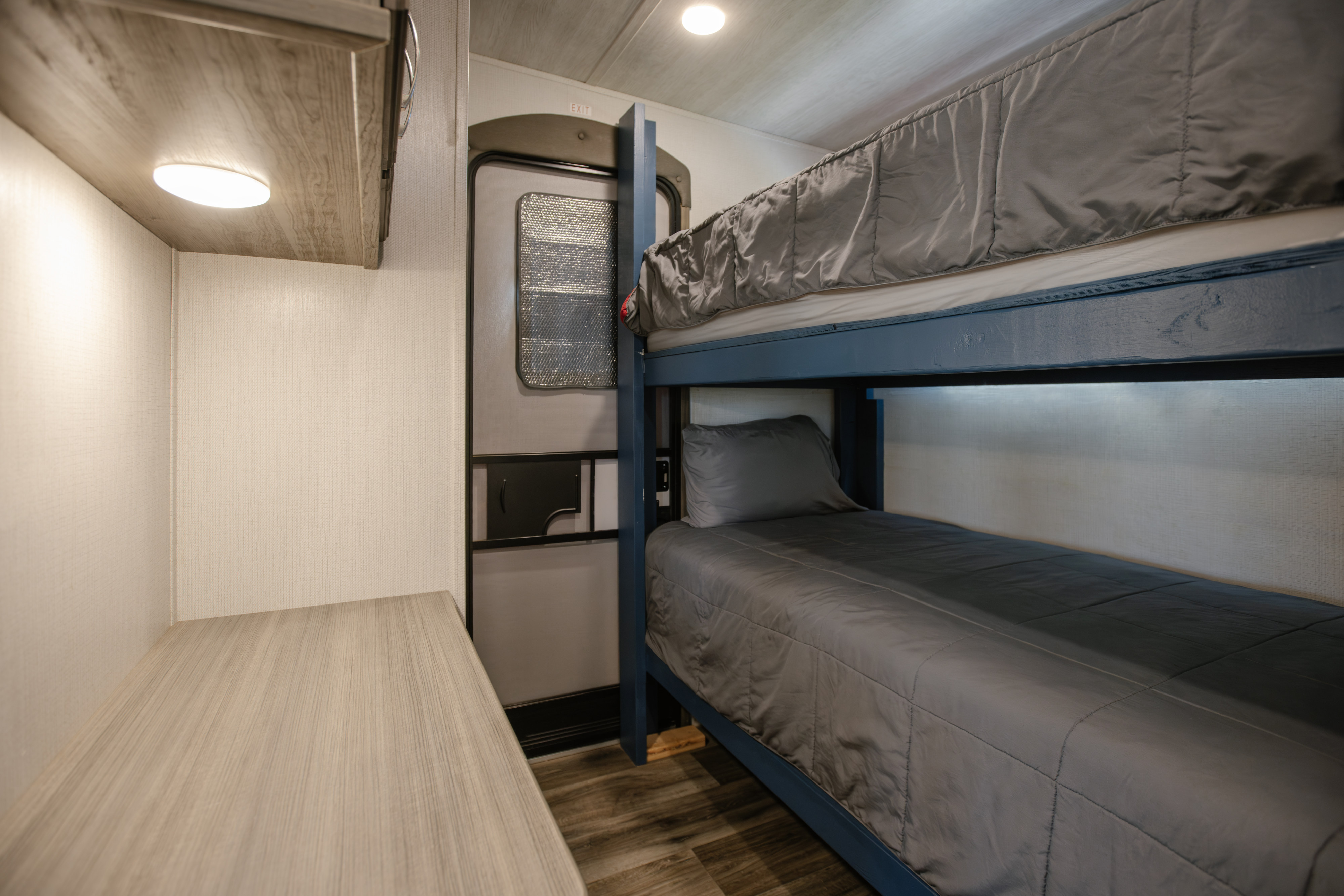 RV rental interior: lower and upper bunk beds with grey bedding, a side desk, and exit door, ideal for trips.. Keystone Cougar 2022