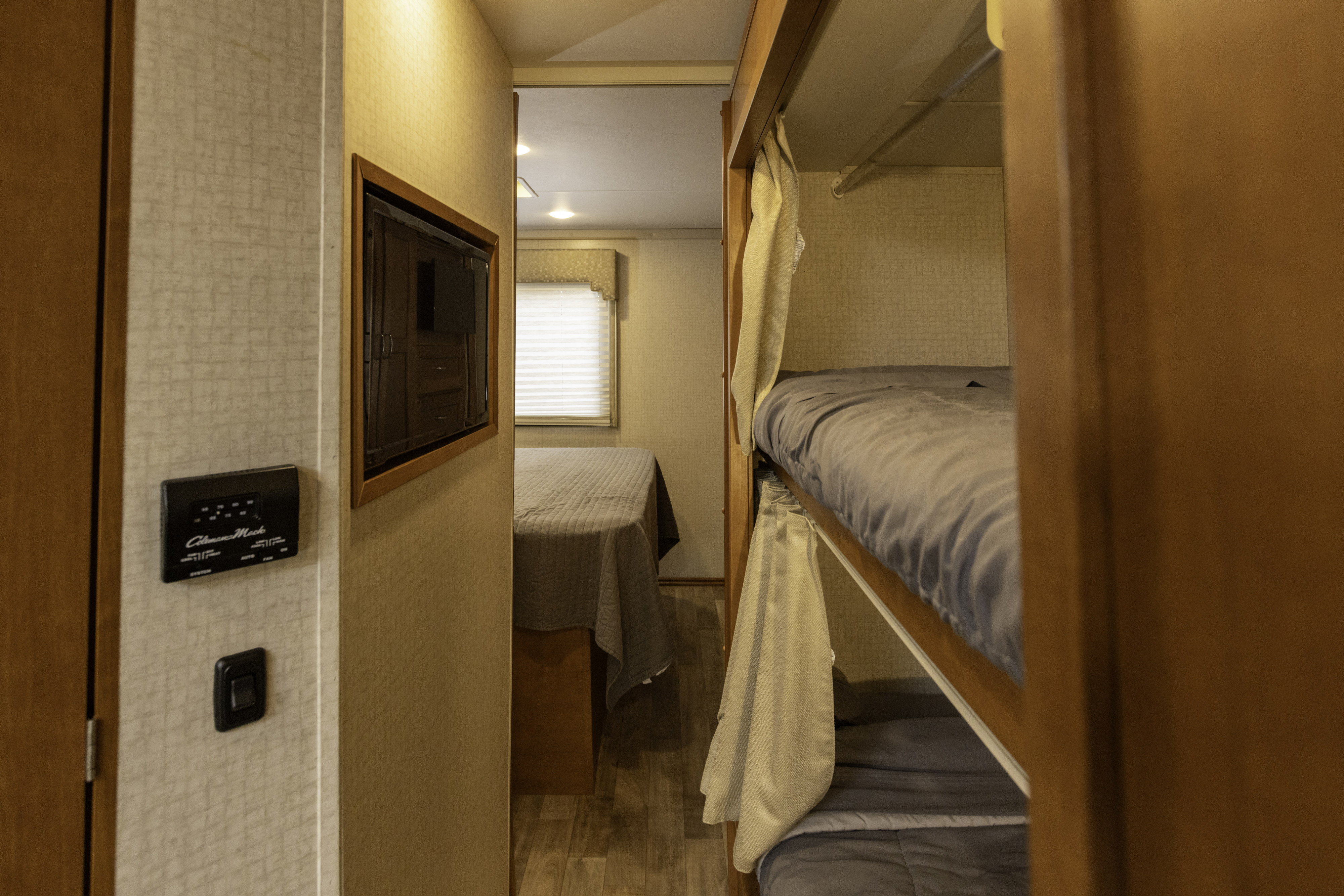 The interior of an **RV rental** shows a narrow hallway with a thermostat, leading to a back bedroom and bunk beds on the right.. Winnebago Spirit 2018