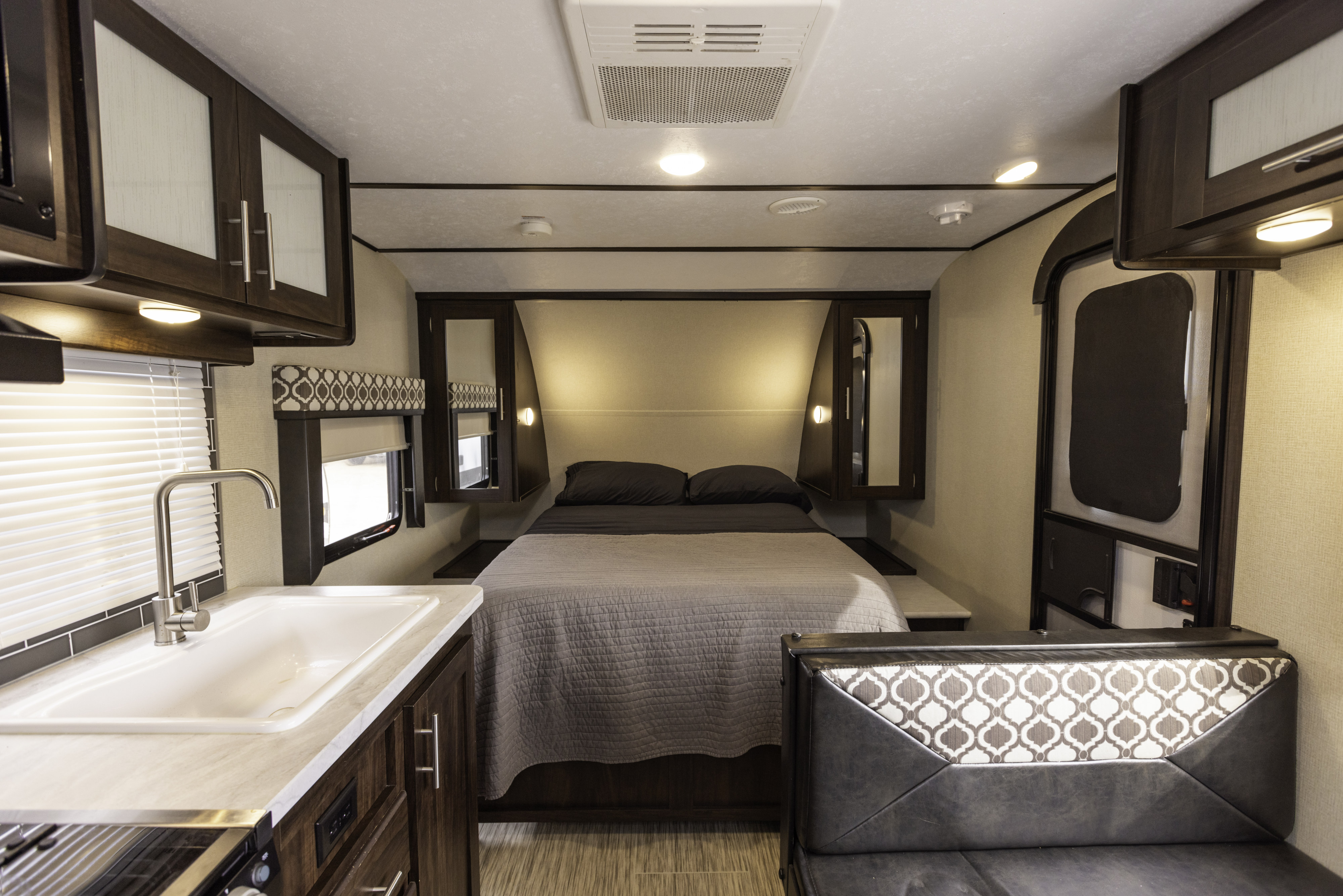 Cozy RV rental interior showcasing a comfortable bedroom, compact kitchen with sink, and a convertible seating area.. Prime Time Tracer 2020