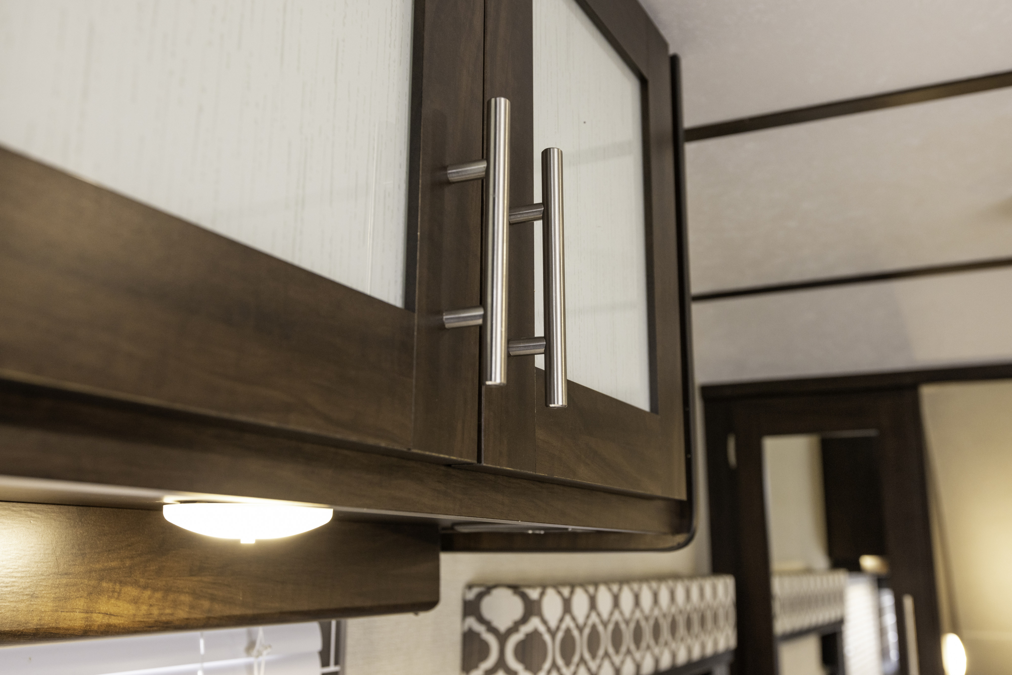 Modern RV rental interior: dark wood overhead cabinets with glass panels, sleek silver handles, and bright lighting.. Prime Time Tracer 2020